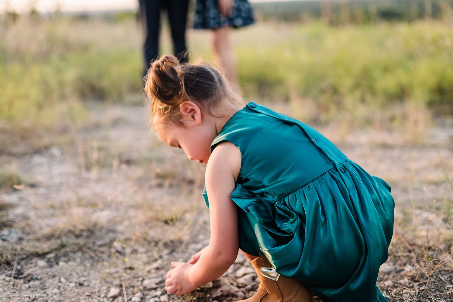 Child in teal dress crawling and exploring outdoors in natural setting.