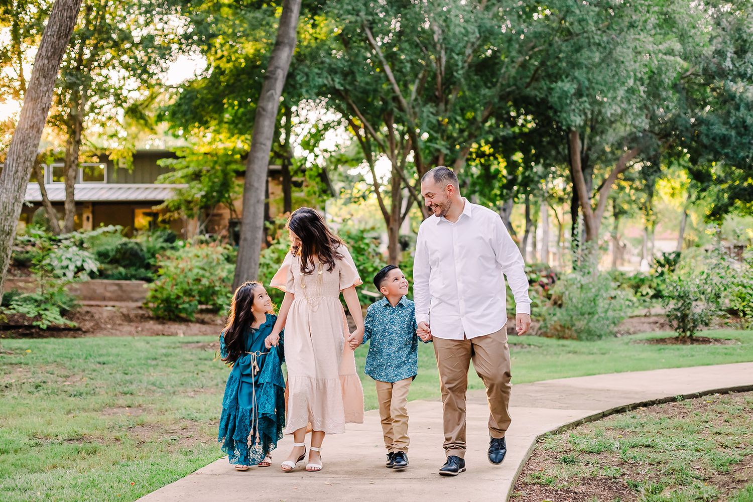 A family walking together through a sunlit park pathway wearing coordinated casual outfits.