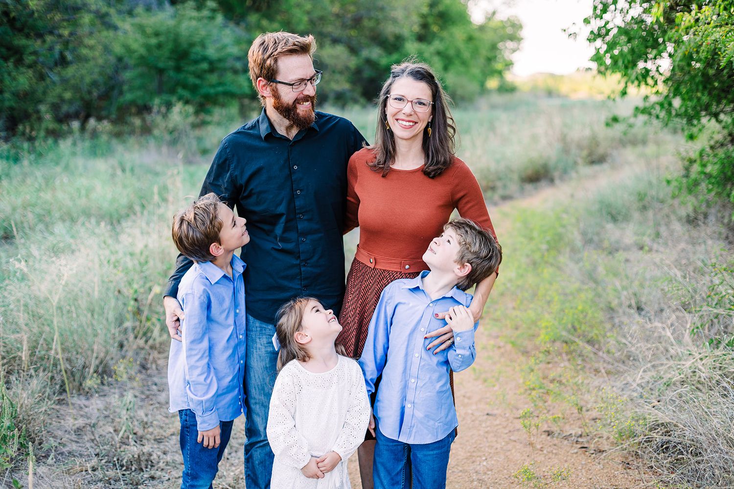 Family standing together on a nature trail surrounded by green foliage.