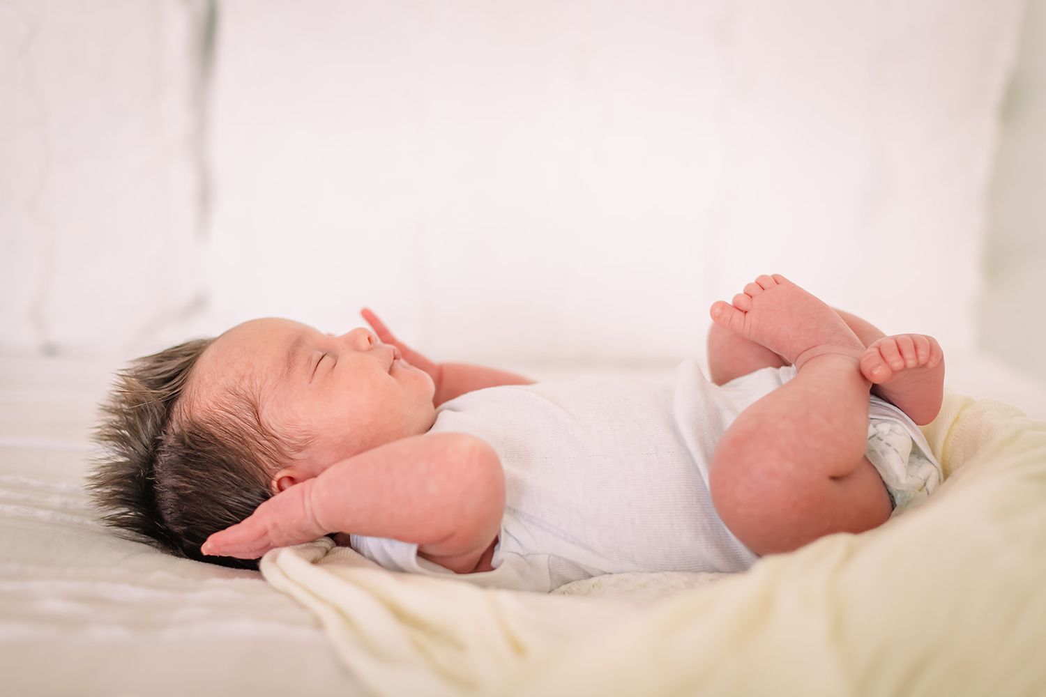 A sleeping baby lies on white bedding with bare feet visible in a soft and peaceful pose.