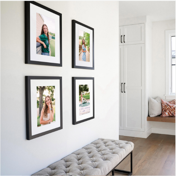 Gallery wall with black framed photos displayed along a white hallway with built-in storage cabinets.