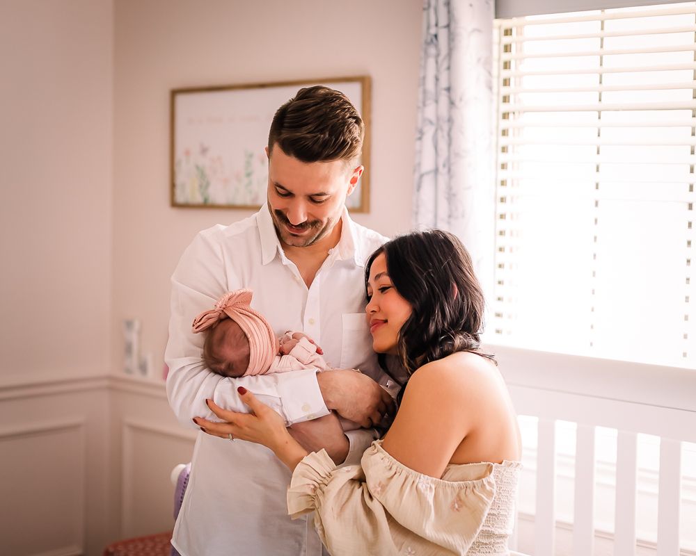 New parents sharing tender moment with newborn baby in nursery with natural lighting.