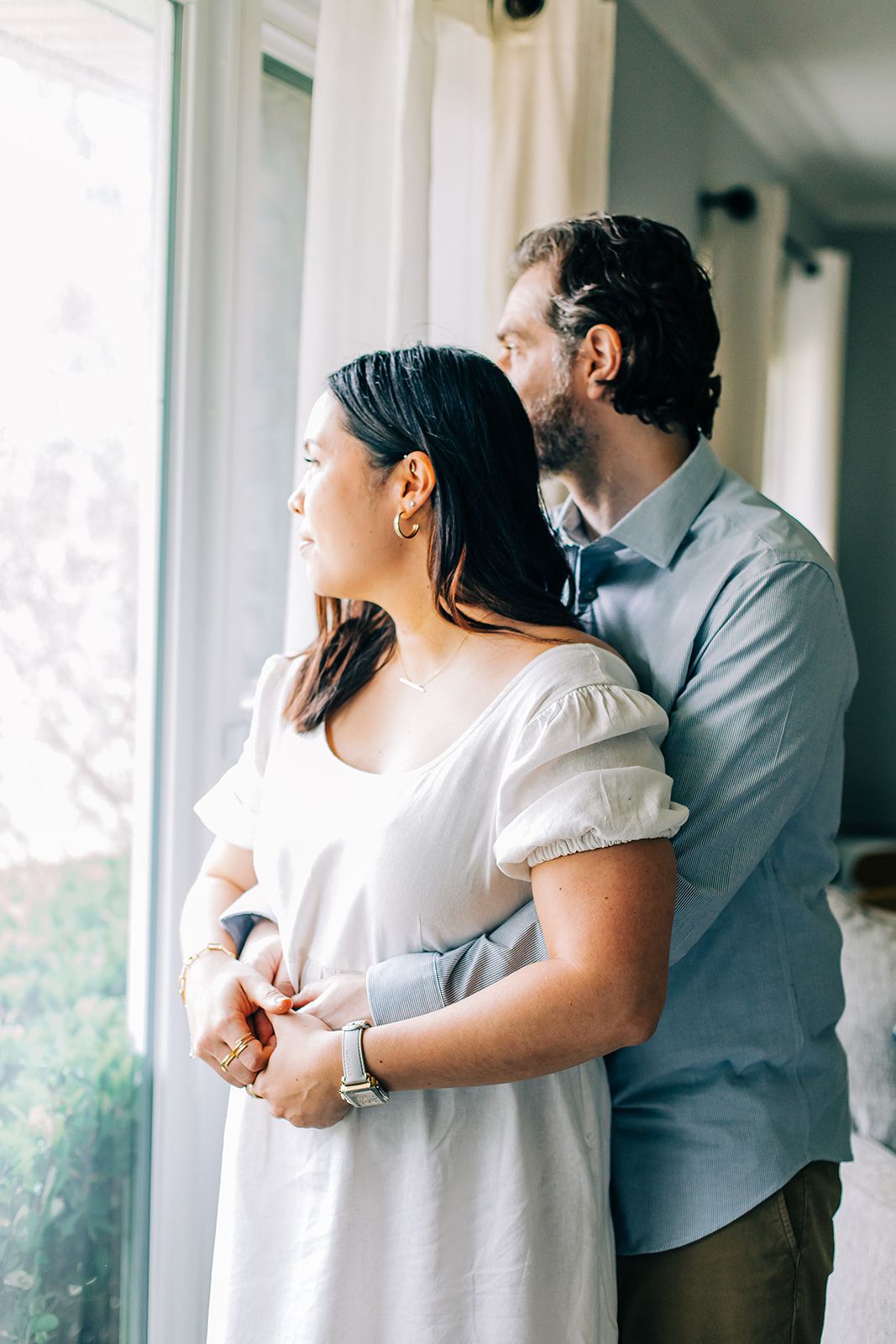 A couple embraces in front of bright windows during an intimate indoor photo session.