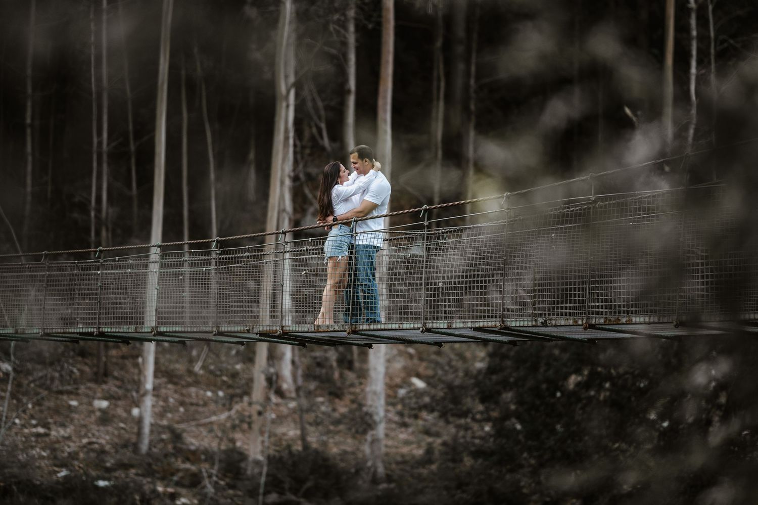 A couple walks hand in hand through a misty wooded path wearing casual attire.