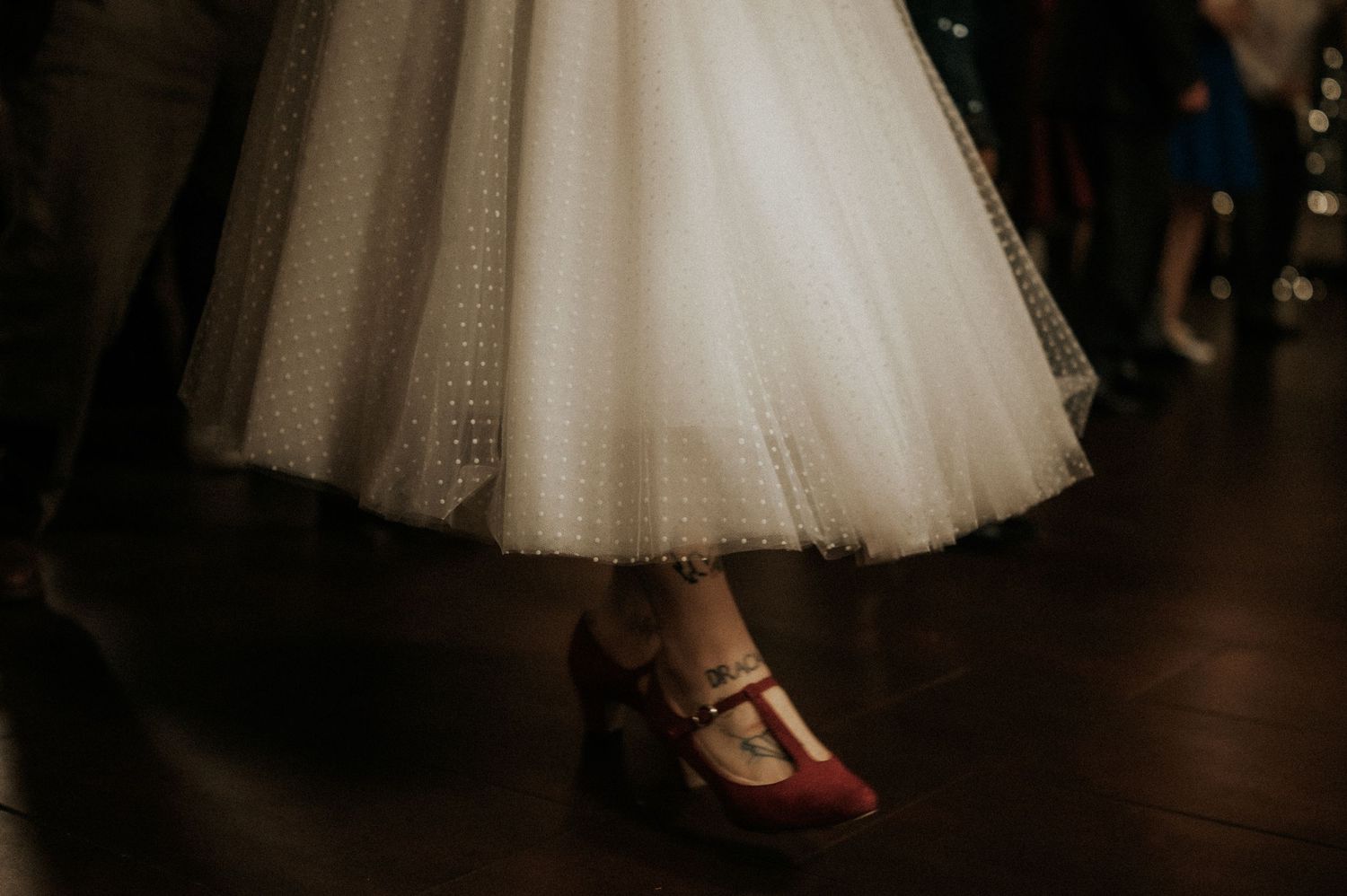 White tulle skirts and red shoes are displayed in a dimly lit dance performance setting.