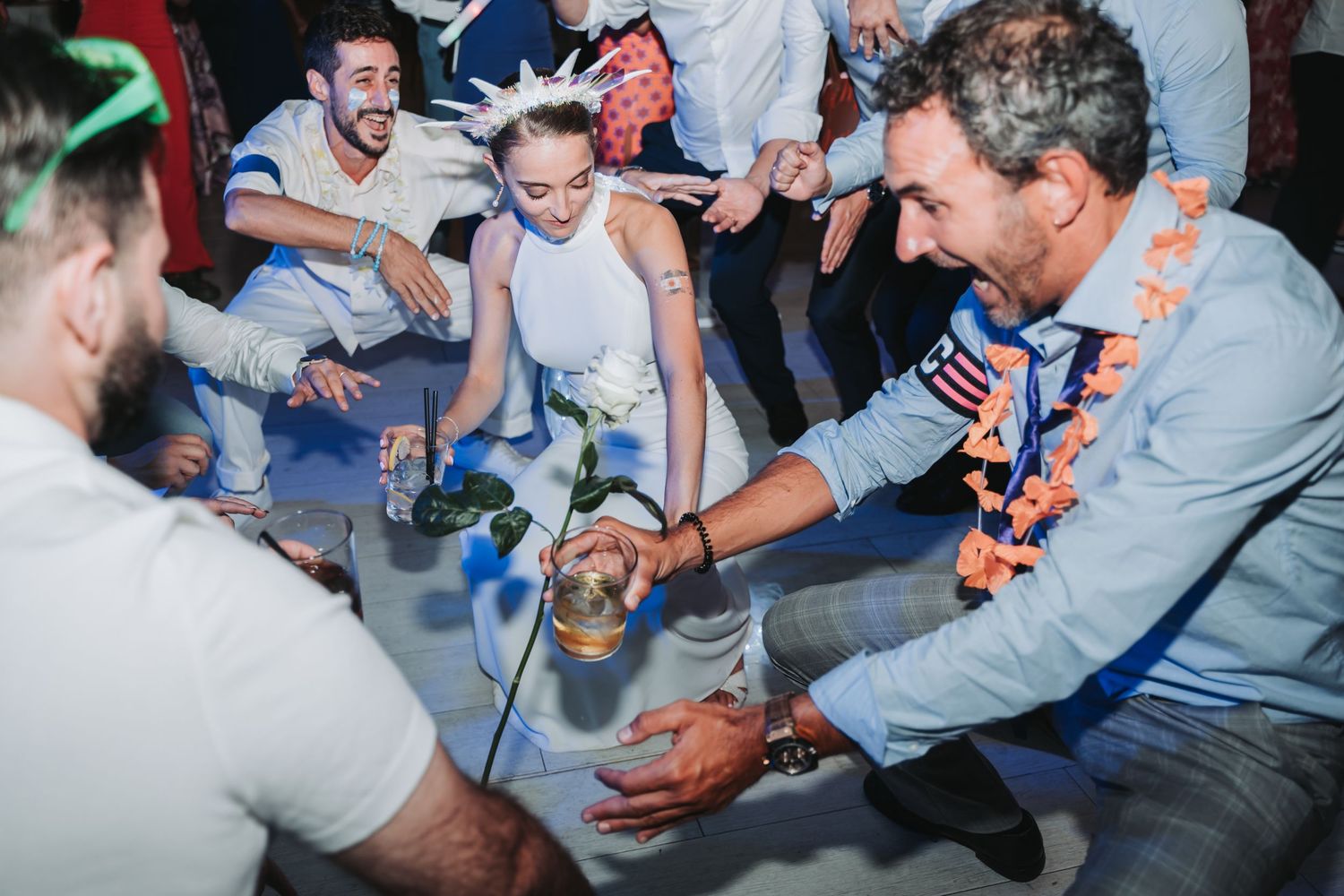 Wedding guests enjoying drinks and dancing at a lively reception party with festive lighting.