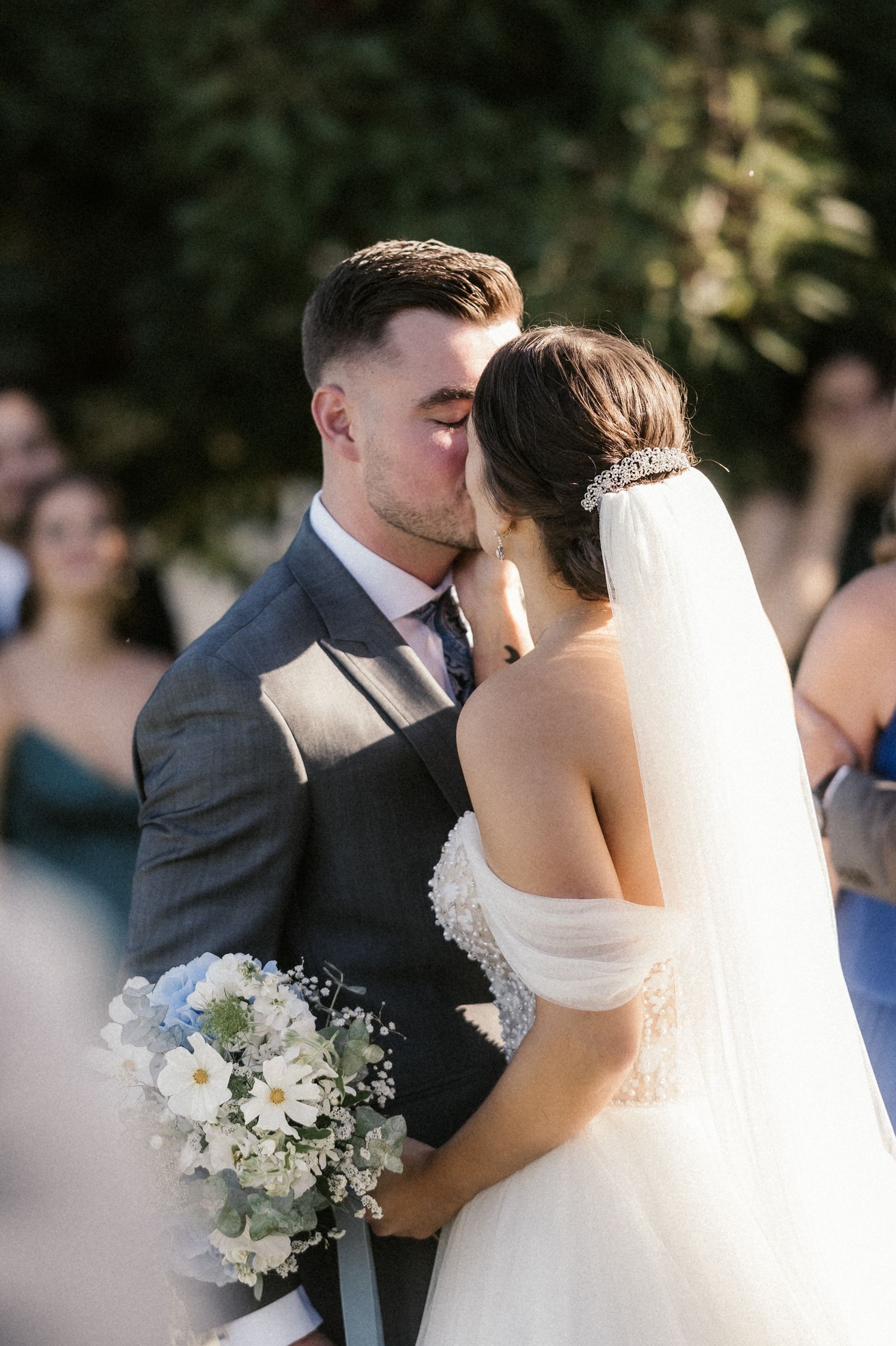 A romantic wedding moment captured as newlyweds share a kiss while the bride holds a white floral bouquet.