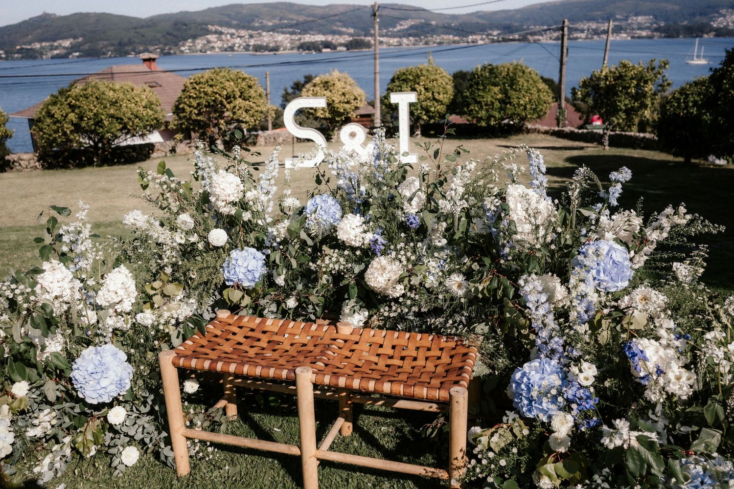 A scenic coastal wedding venue decorated with white floral arrangements and wooden pergolas overlooking the ocean.