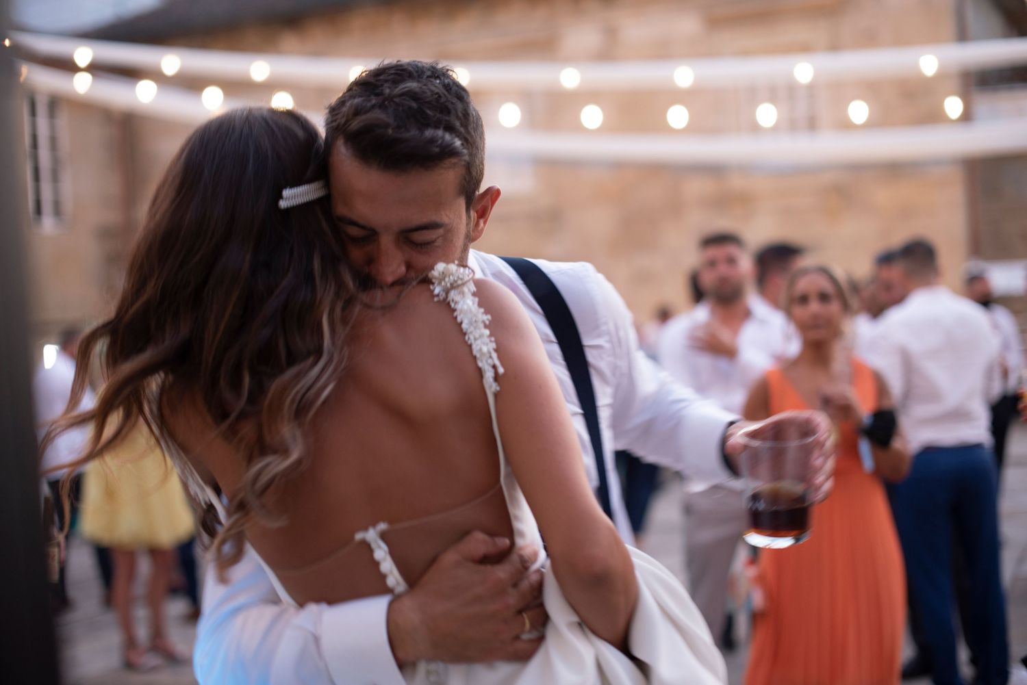 Wedding reception guests dance under string lights at an outdoor venue.