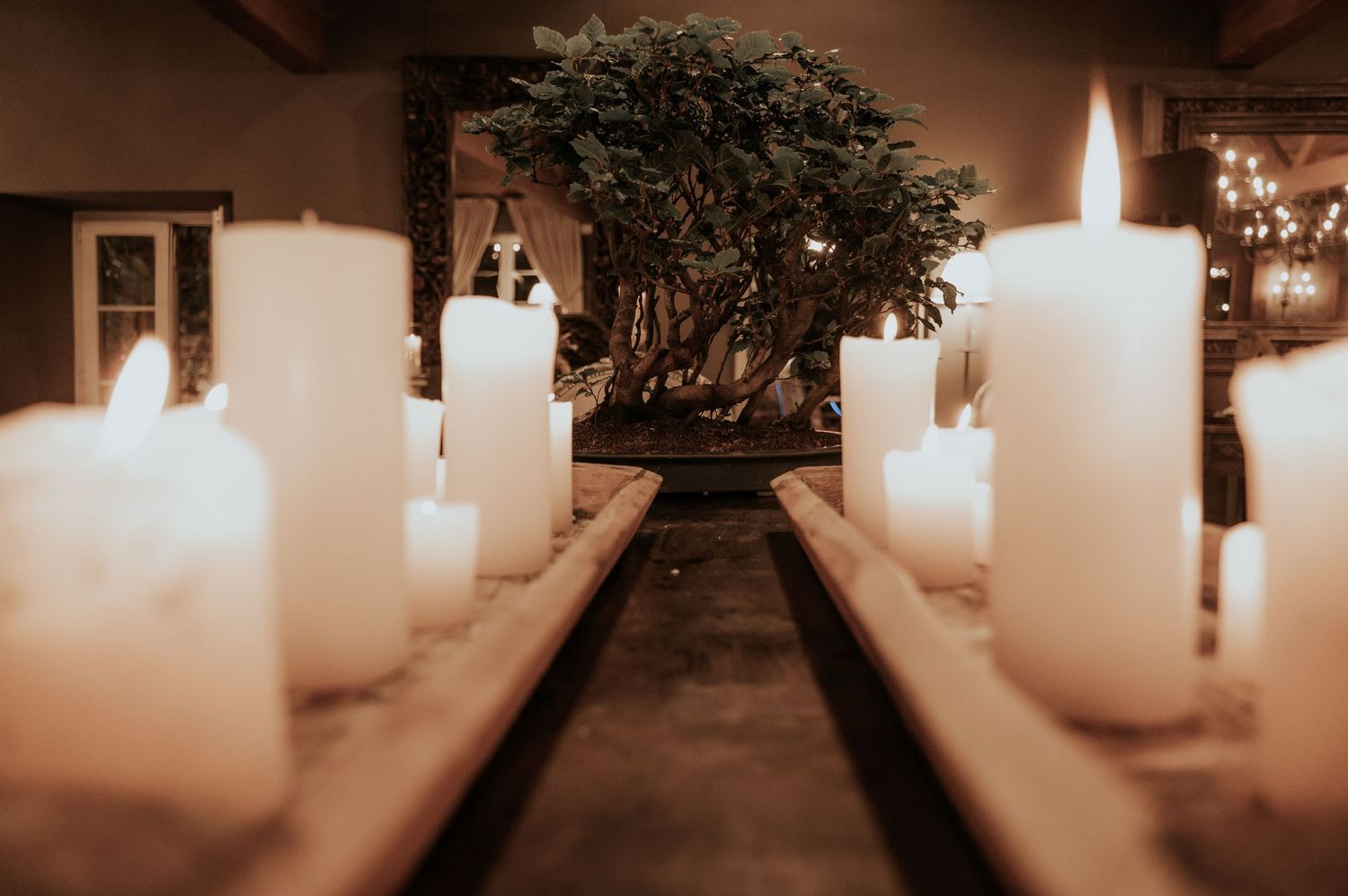 A row of glowing white pillar candles creates a warm and atmospheric pathway in a dimly lit hallway.