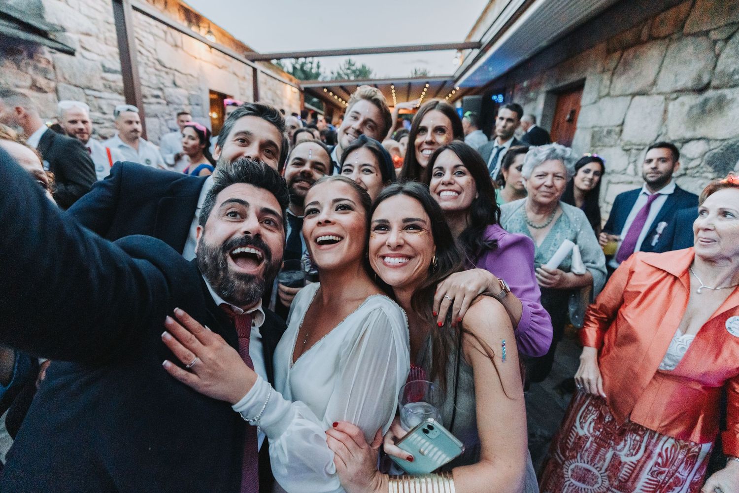 Wedding guests dance and celebrate together at a lively reception party with colorful lighting.