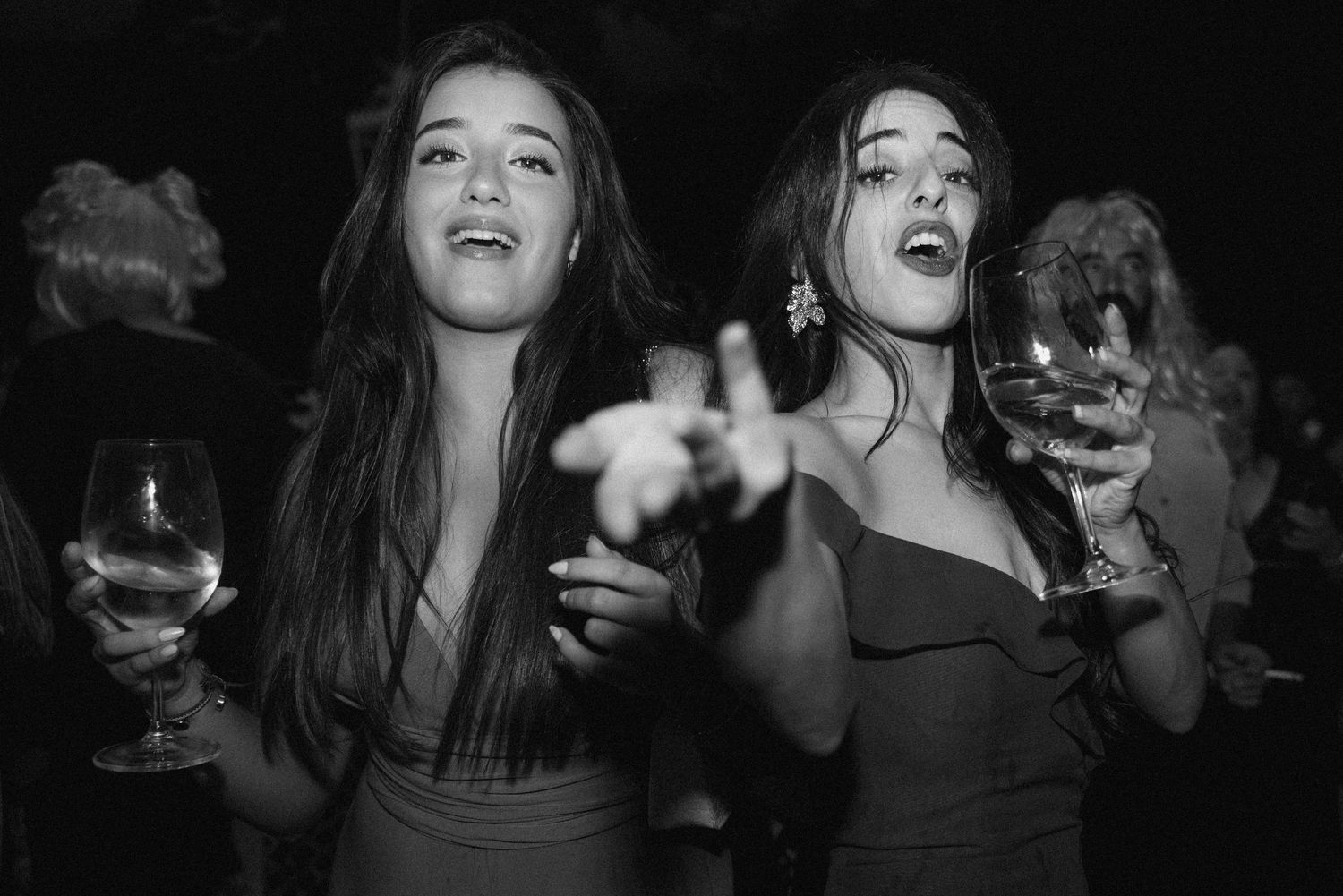 Black and white photo of two women dancing and celebrating with drinks at a nightclub party.