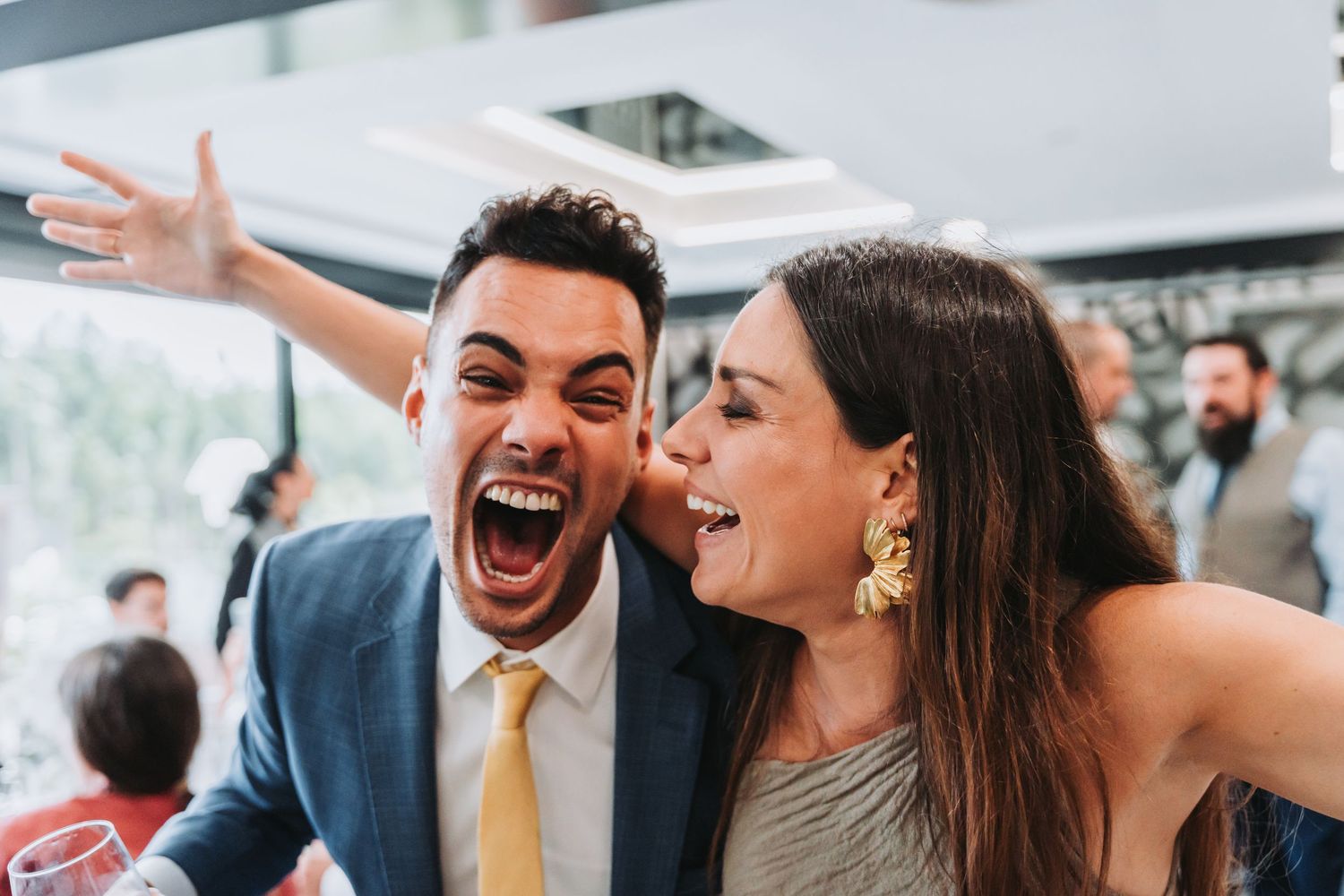 Wedding guests celebrate joyfully on the dance floor at an indoor reception venue.