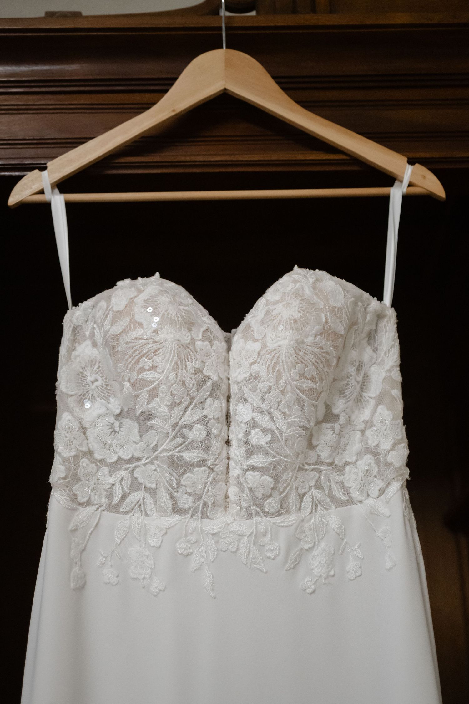 Close-up view of white lace bodice details on wedding dress hangers showing delicate floral embroidery patterns.