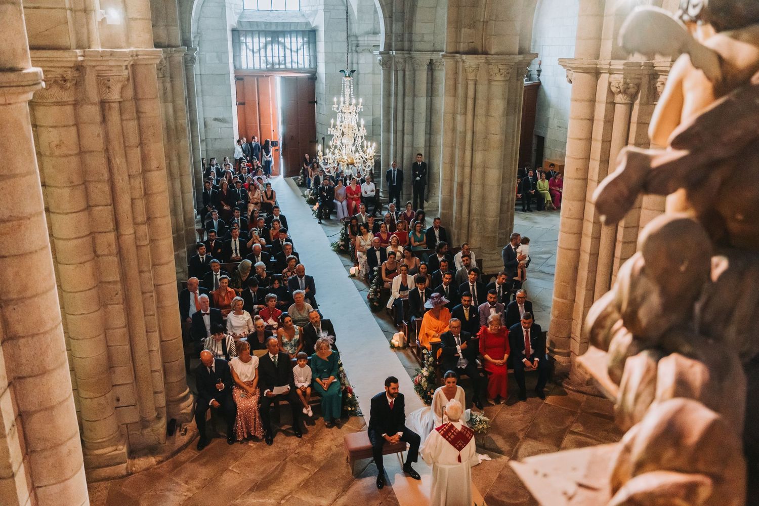 Wedding guests gathered in a grand stone church interior with tall architectural columns.