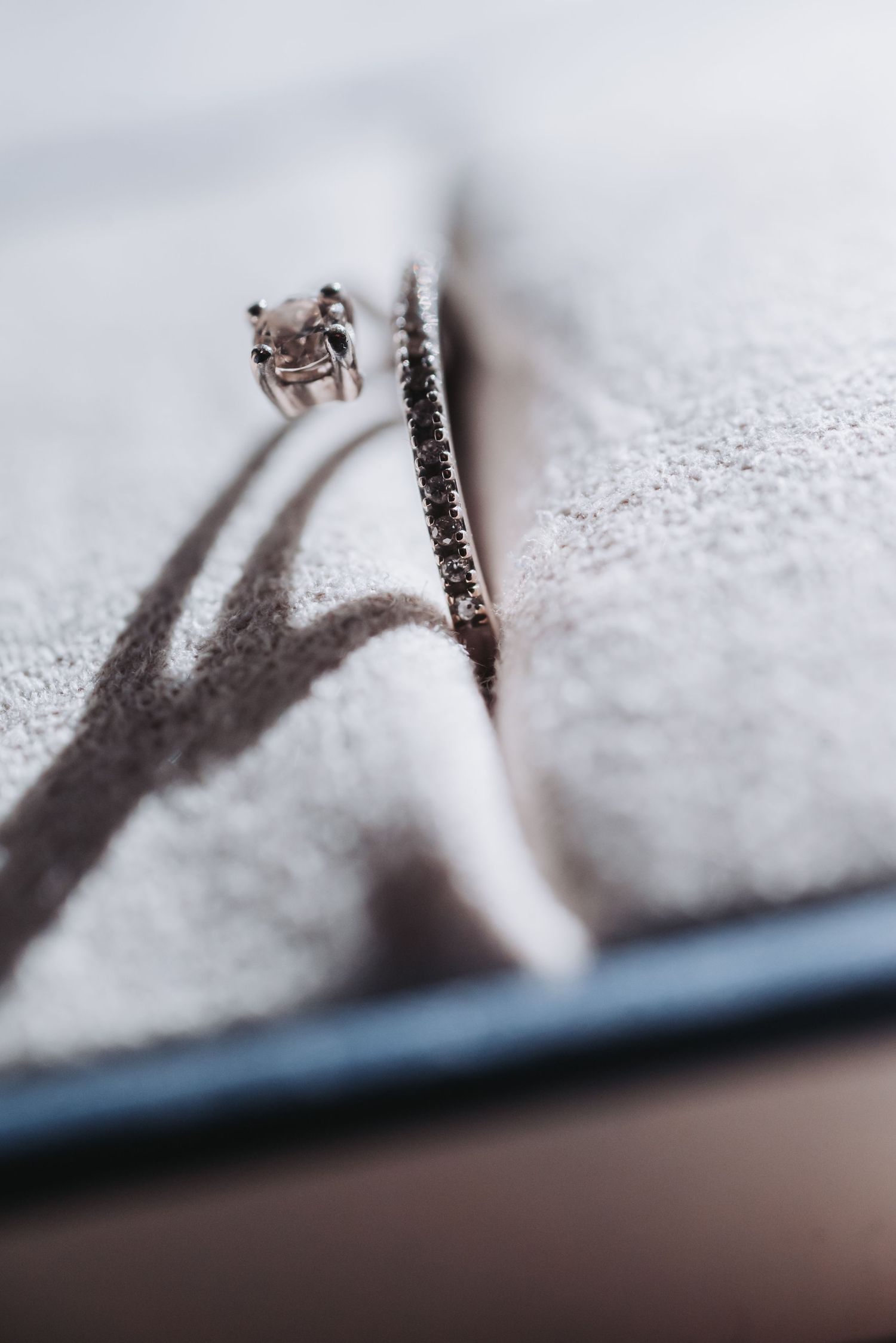 Close-up macro shot of an elegant diamond engagement ring casting shadows on a textured white surface.