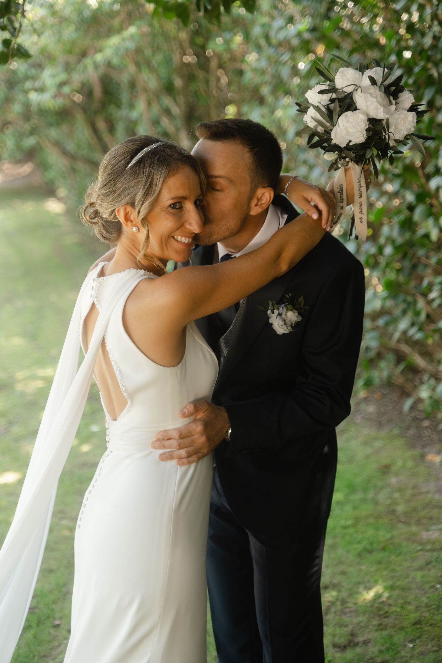 A romantic wedding couple embraces in a garden setting with natural greenery and soft lighting.