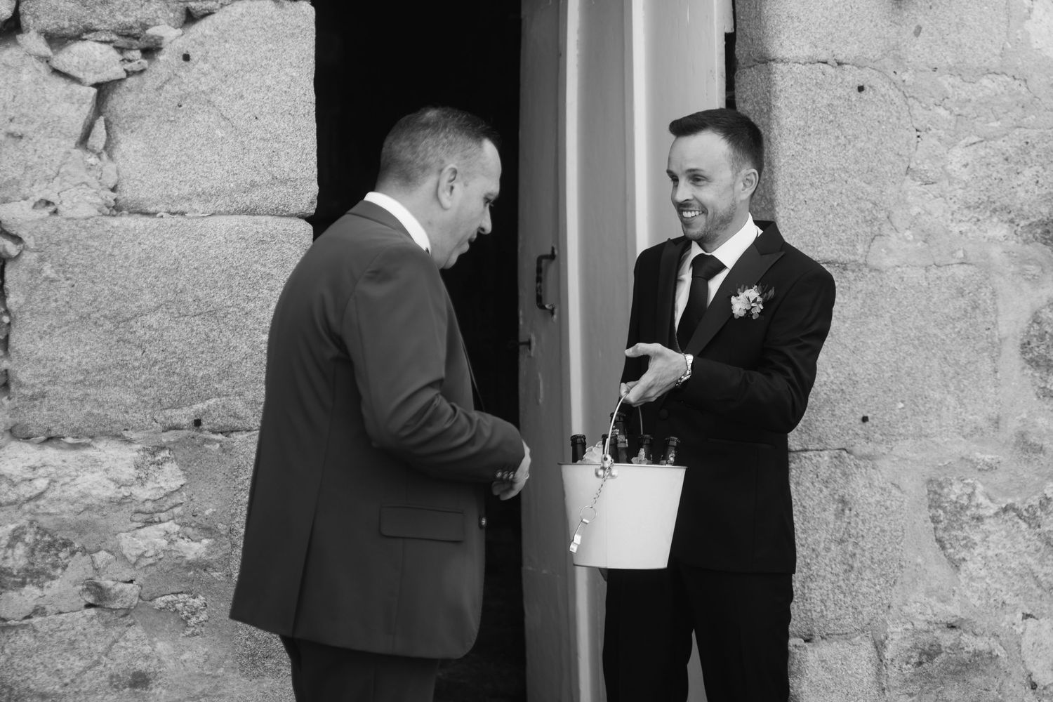 Two people in formal attire engage in conversation while standing by a doorway in black and white photography.