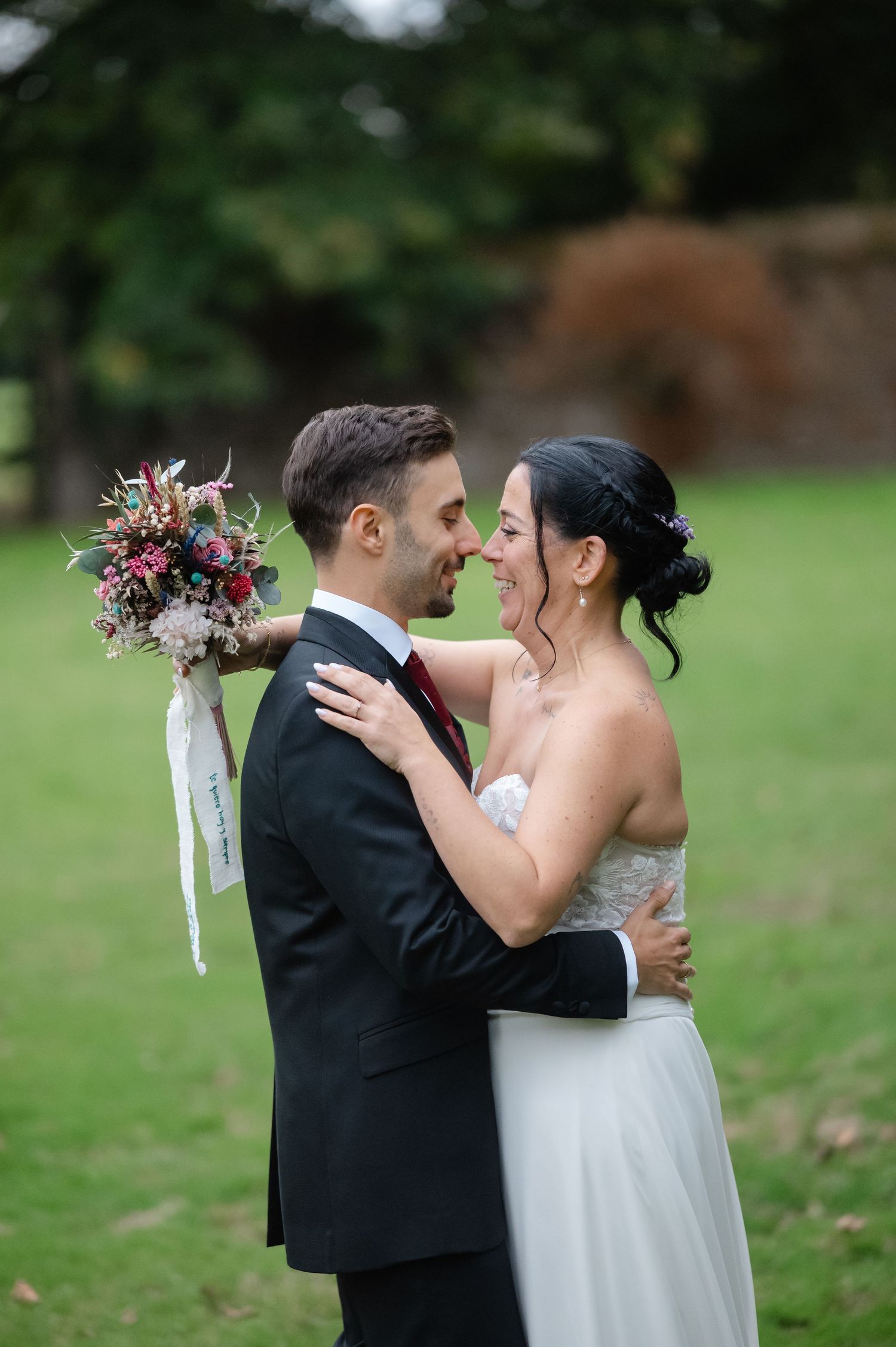 A romantic wedding moment captured outdoors with a beautiful bouquet featuring pink and purple flowers.
