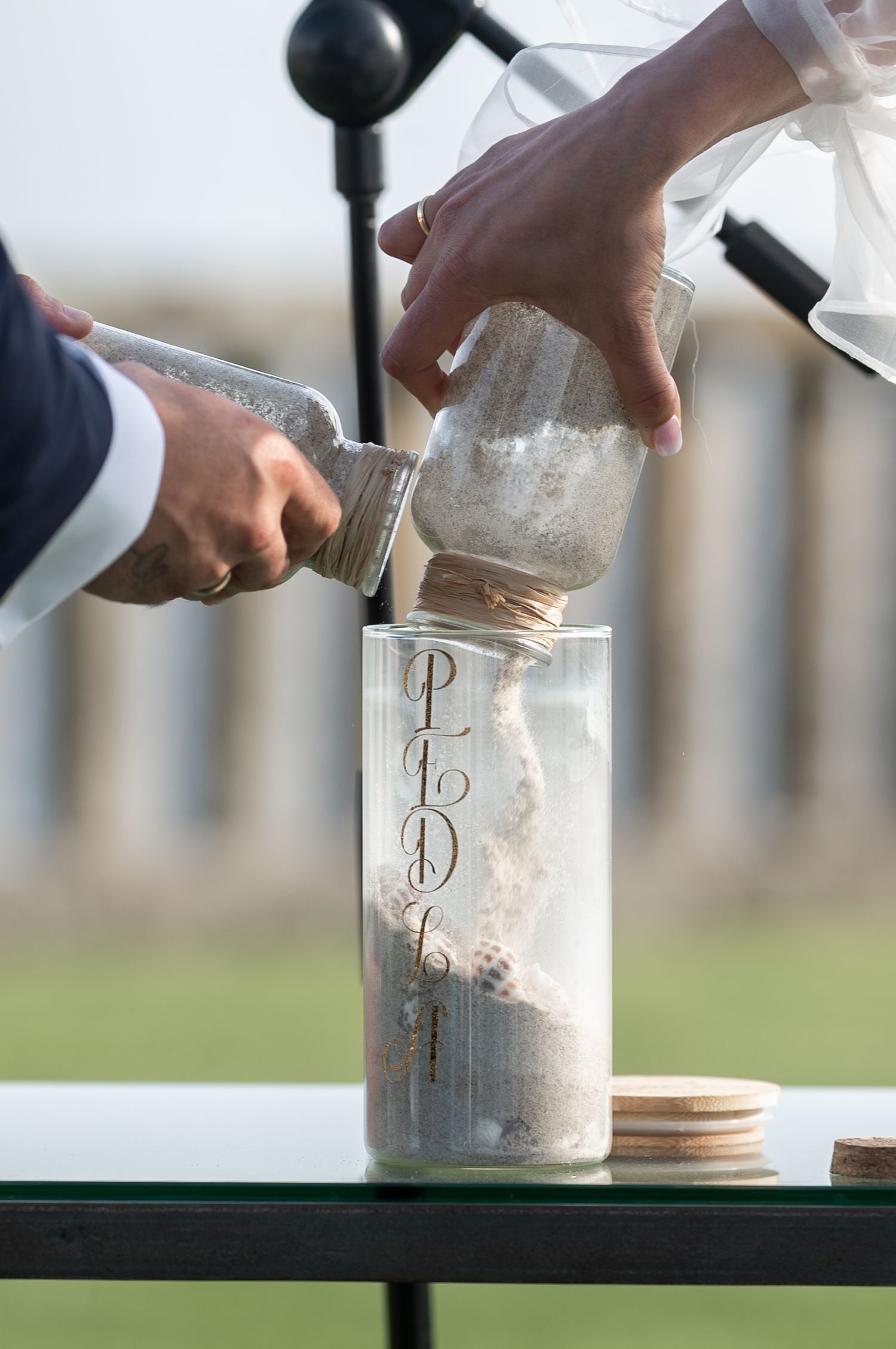 Close-up shots of hands pouring sand into a decorative jar during a unity sand ceremony at a wedding.