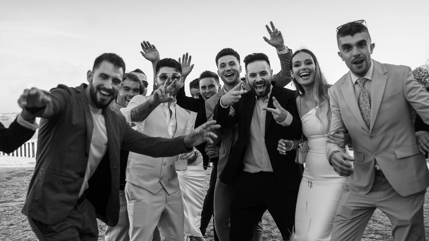Black and white panorama of wedding guests cheering and raising their hands in celebration.