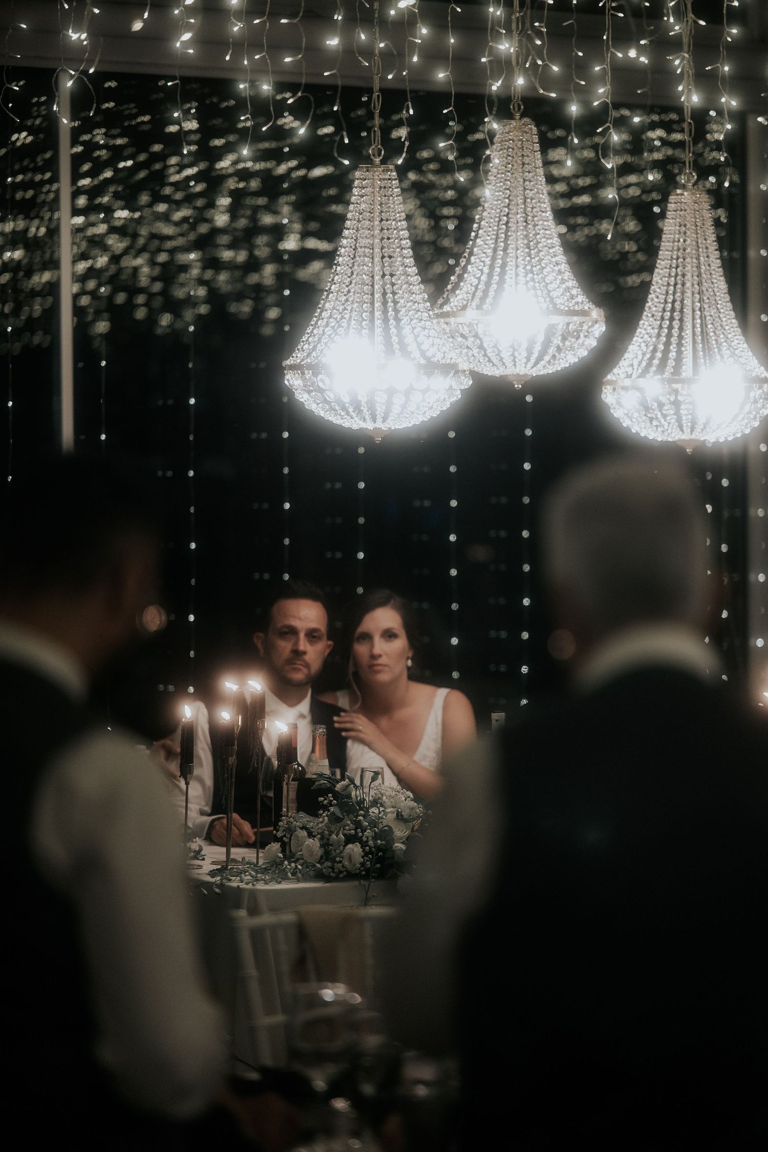 Elegant crystal chandeliers illuminate a dark reception venue with twinkling lights creating a romantic ambiance.