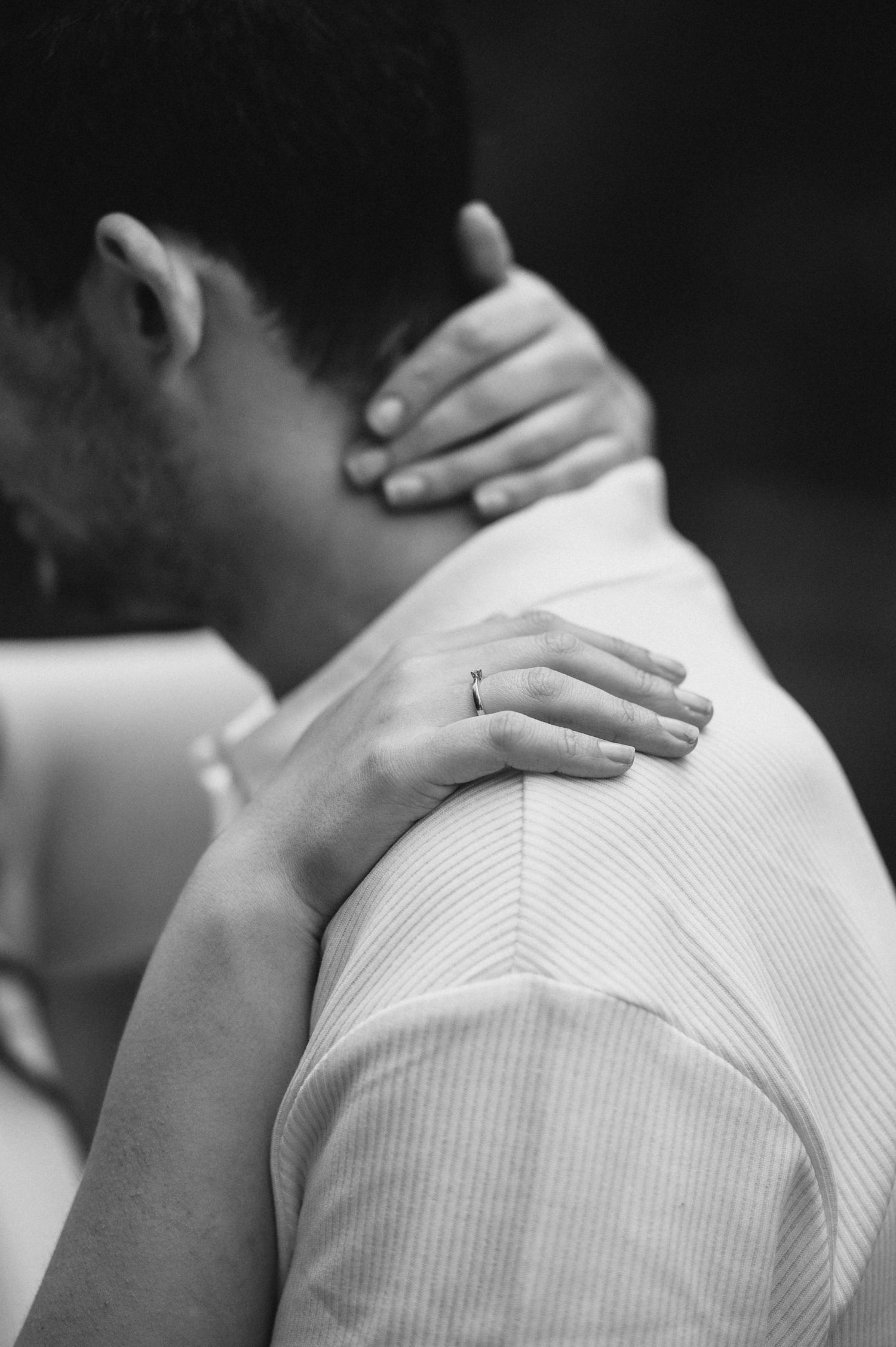 Close-up black and white photo showing hands tenderly placed on shoulders.