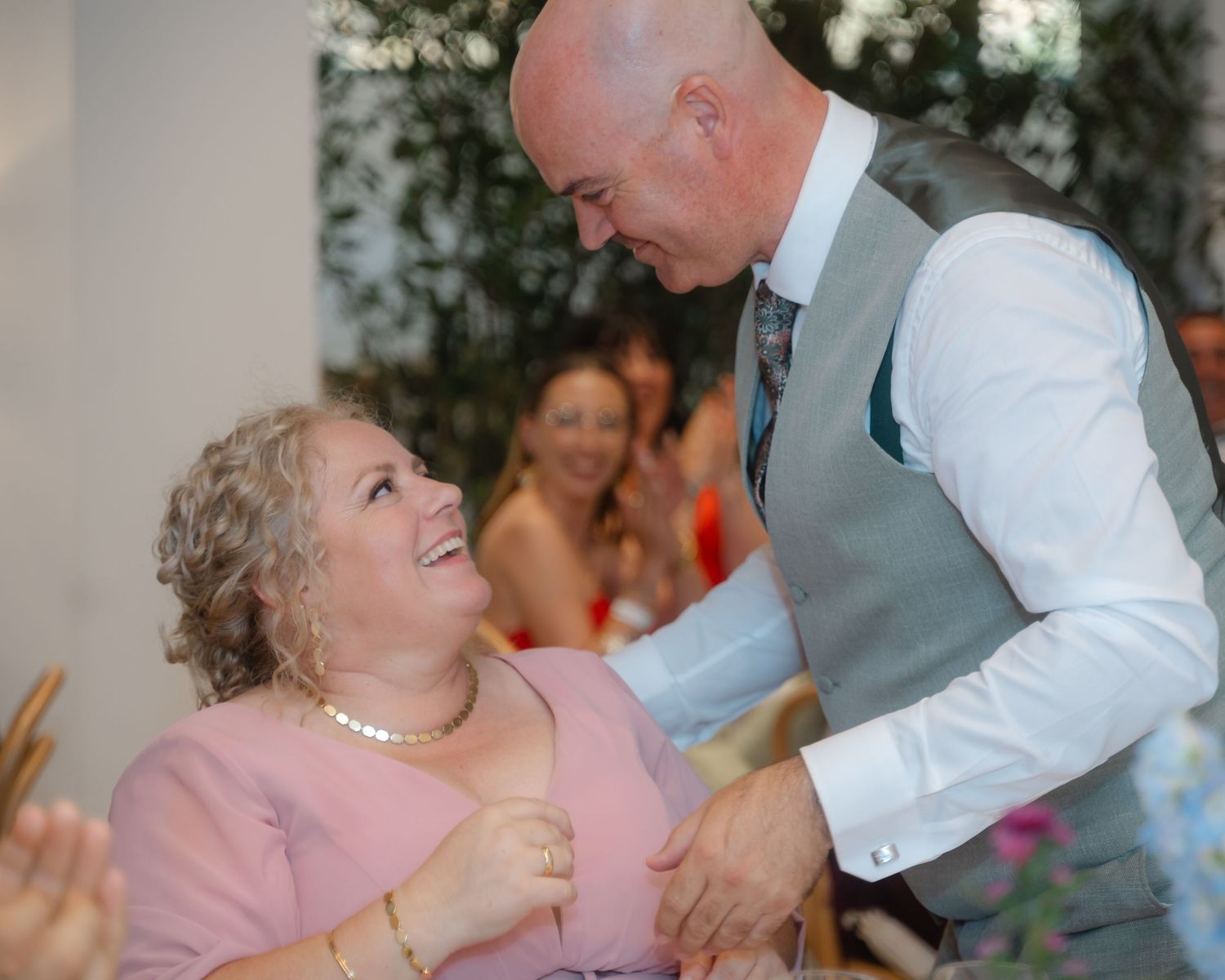 A couple dancing together at a wedding reception, with the woman wearing a pink dress and pearls.
