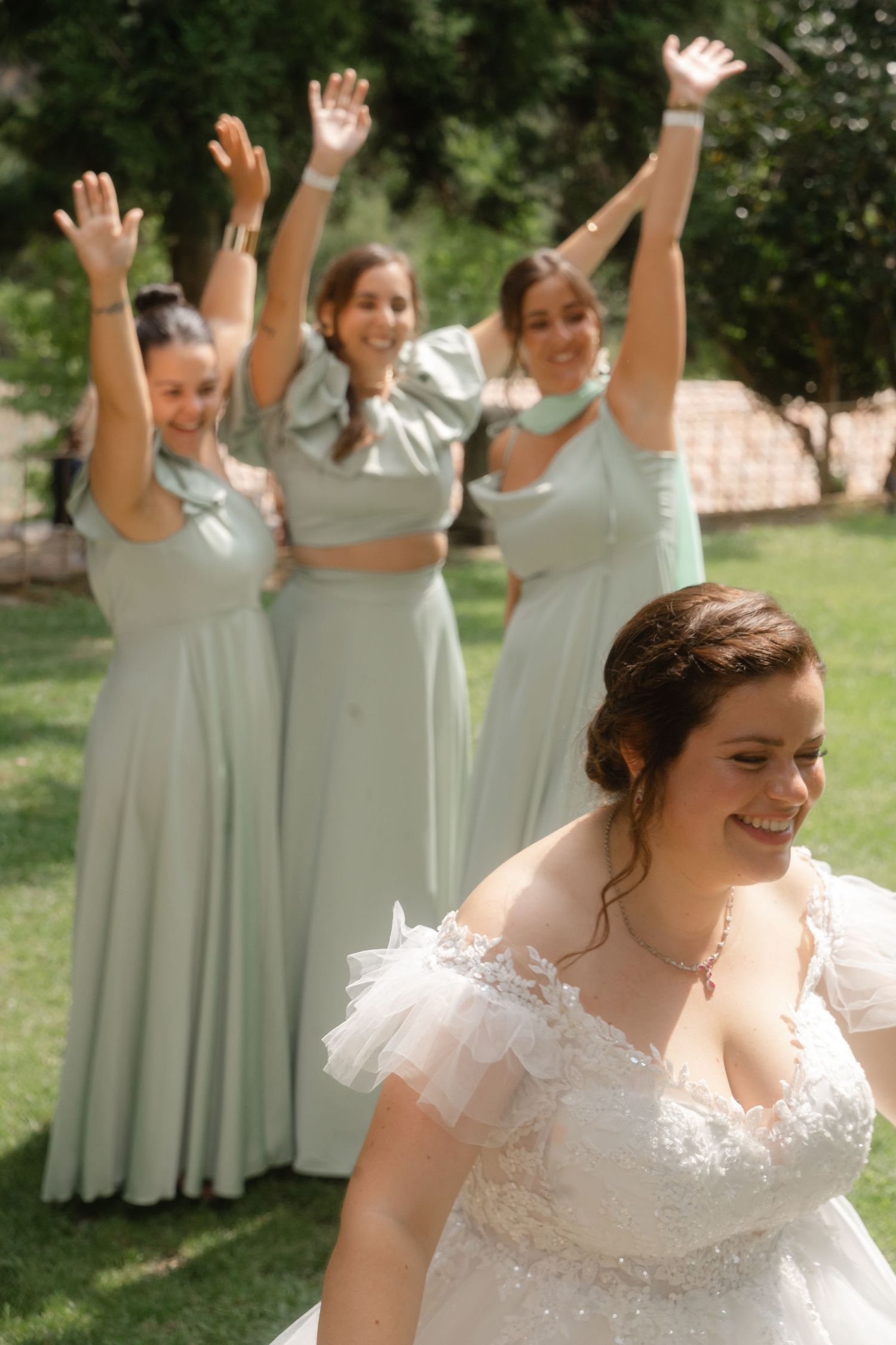 Joyful wedding party poses outdoors with bridesmaids in mint green dresses celebrating with raised arms.