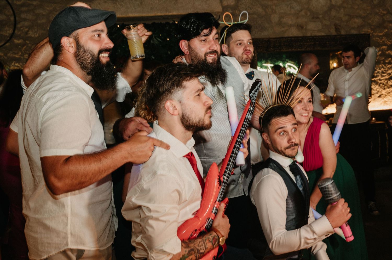 A group of people dance and celebrate with red inflatable instruments at a lively indoor party.