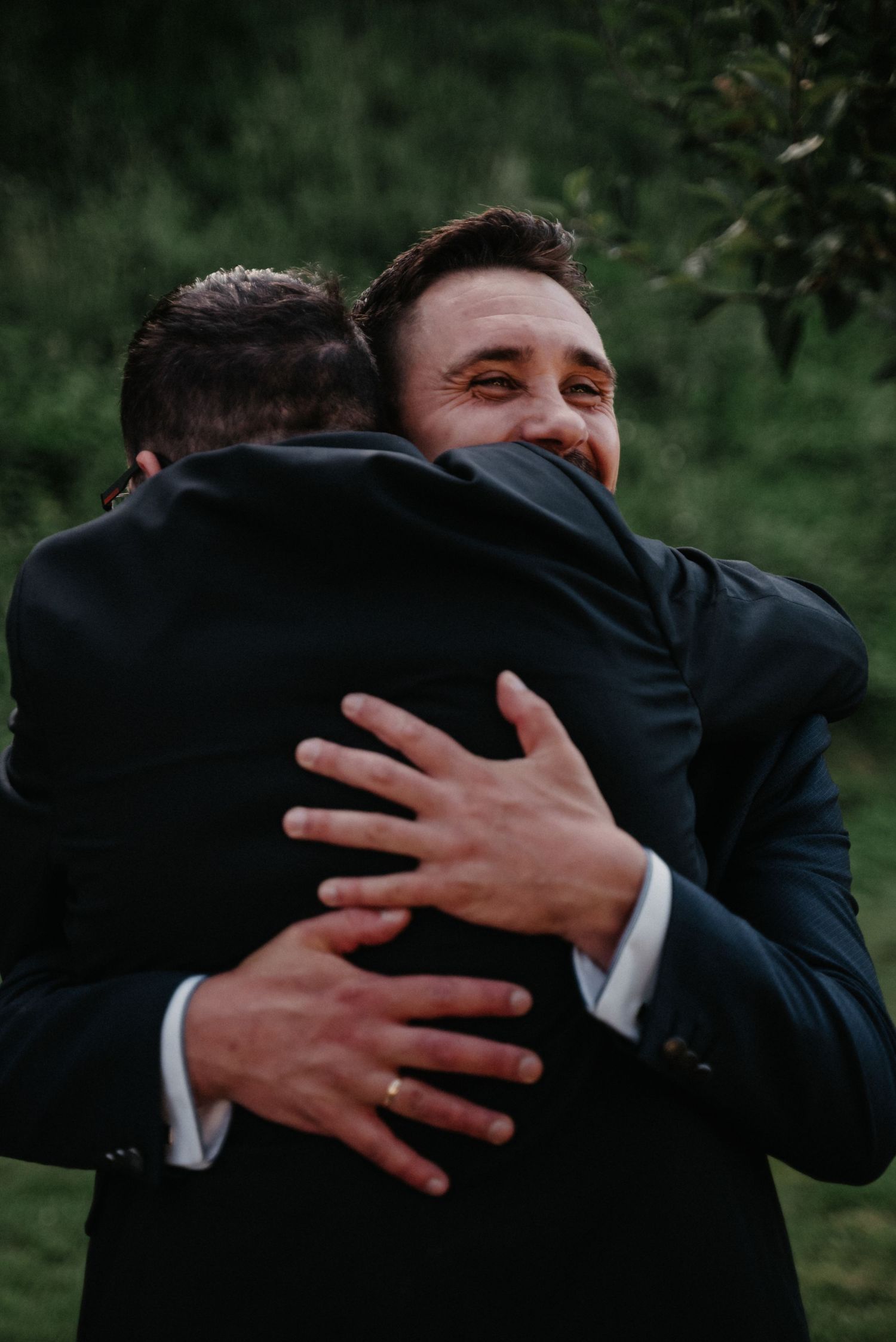 Emotional embraces between men in dark suits during a wedding celebration.