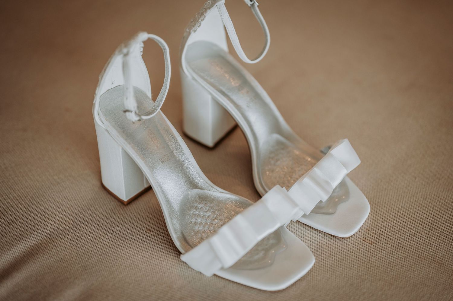 Elegant white platform sandals with block heels and ankle straps displayed against a warm brown background.