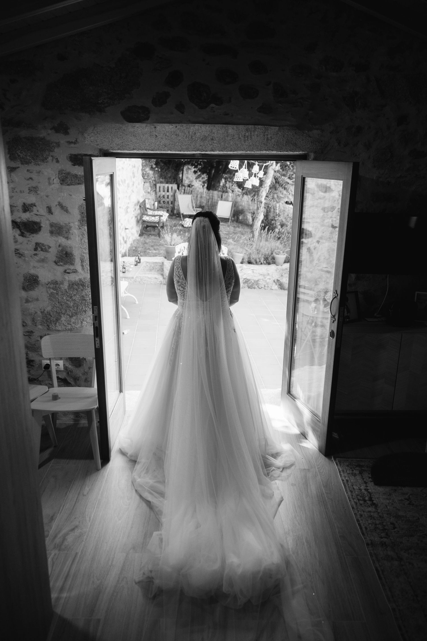 Wedding gown illuminated by natural light streaming through windows in a rustic stone room.