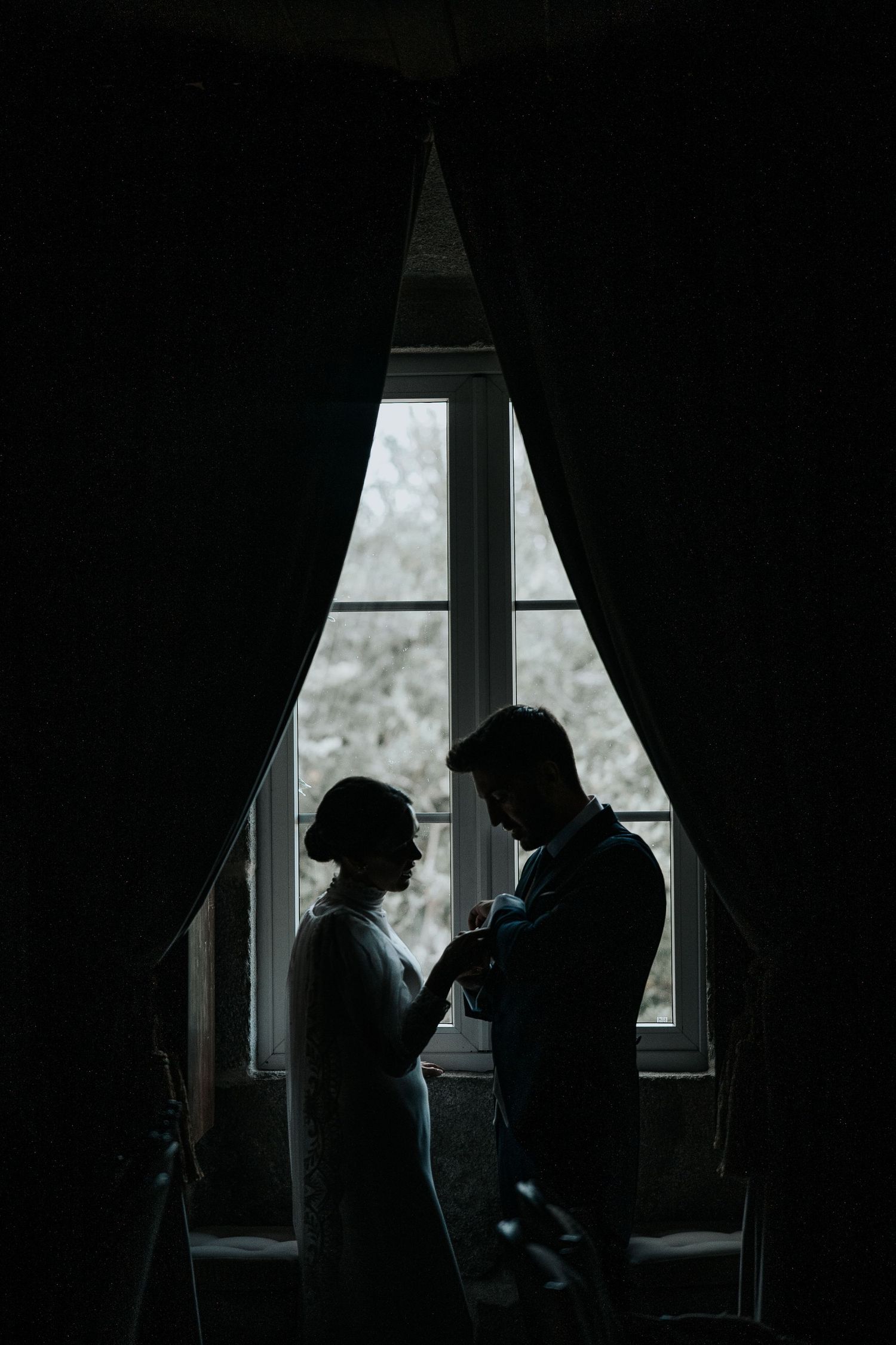 Silhouetted figures stand in dark room near window creating moody atmospheric scene.