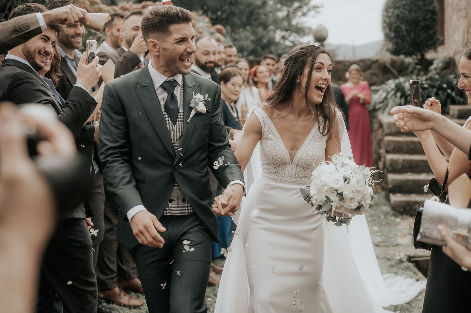 Wedding party and guests gather outdoors for celebratory moments near stone architecture.