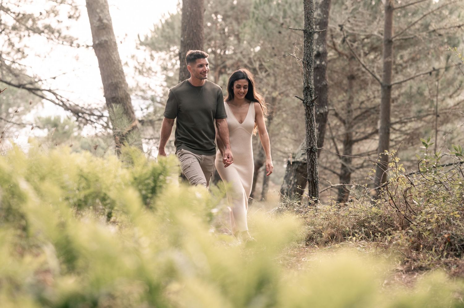 Two people walk together through a scenic wooded trail surrounded by autumn foliage and dappled sunlight.