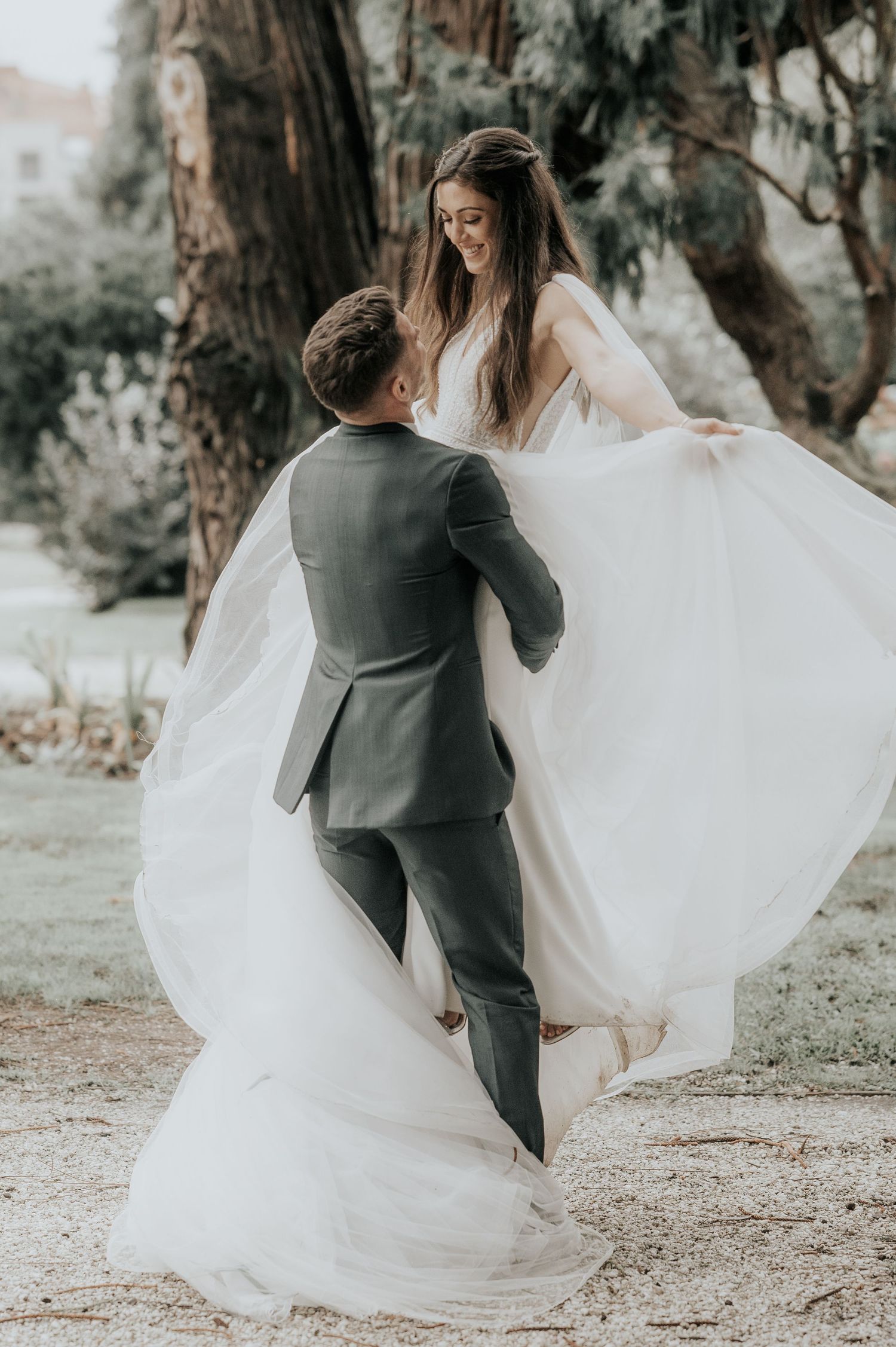 Newlyweds dance together outdoors as bride's white dress flows in the wind.