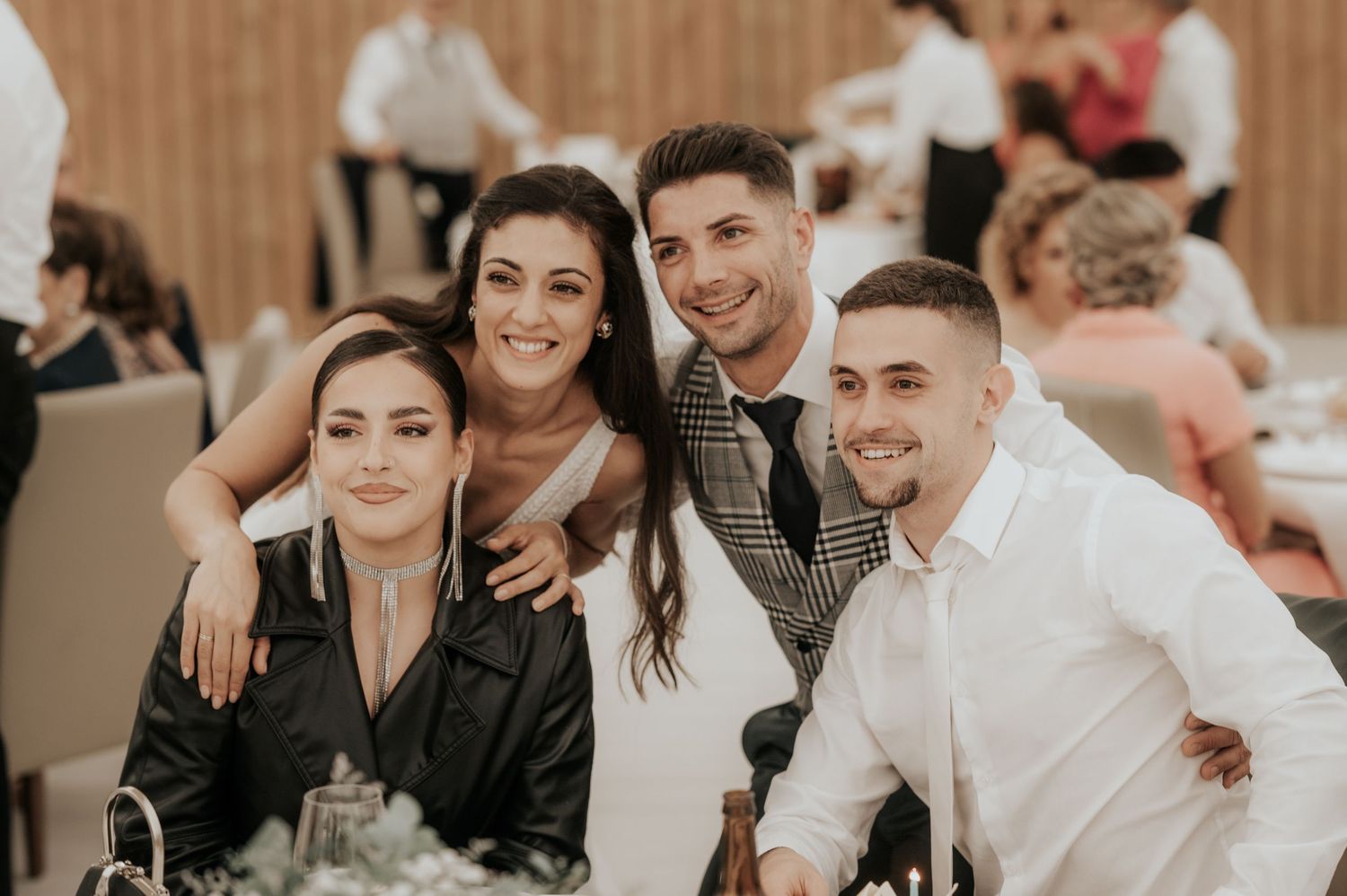 A group of guests enjoying a lively reception celebration with smiles and laughter in an indoor venue.