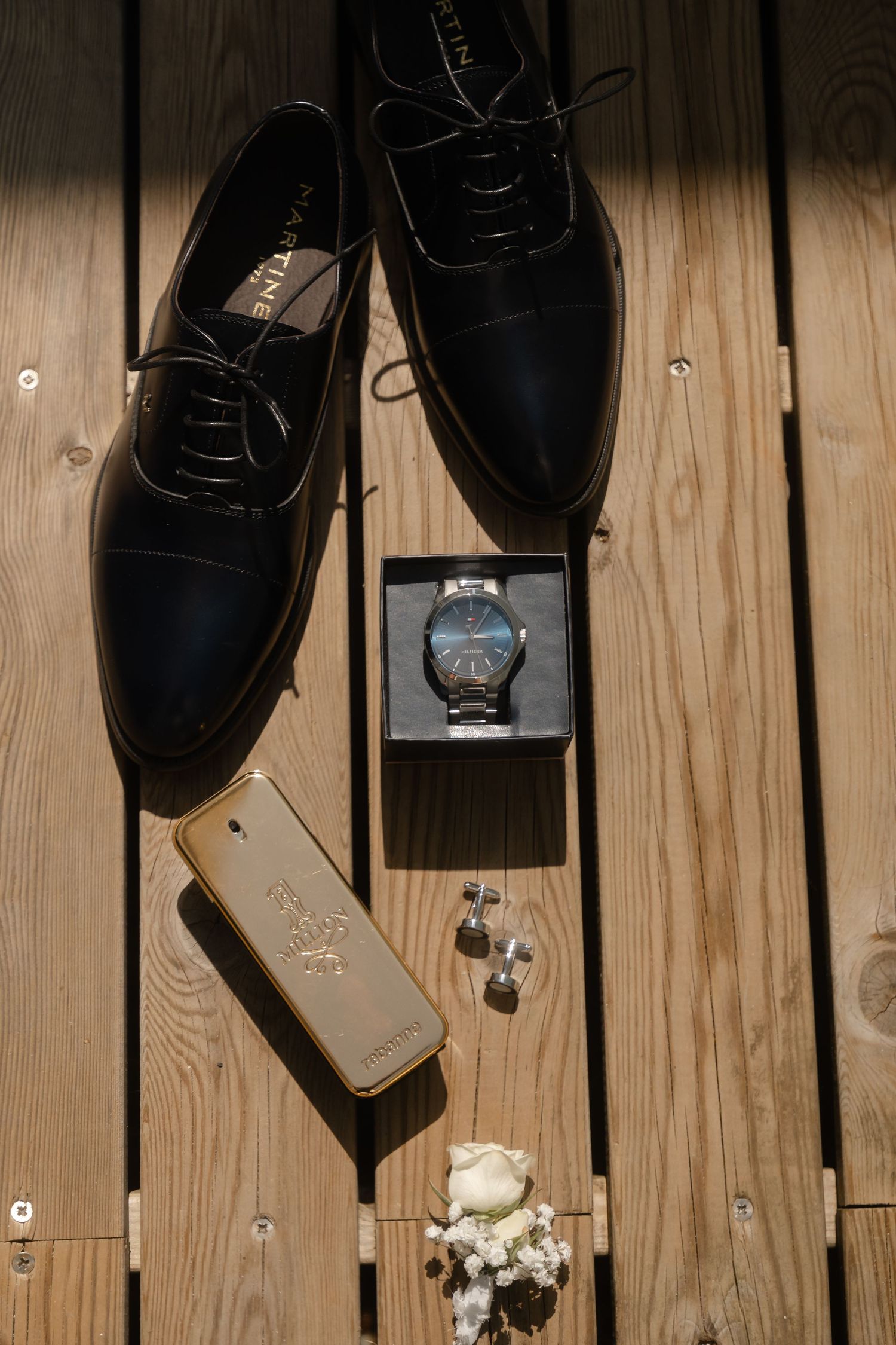 Black formal shoes and accessories arranged on a rustic wooden floor in preparation for a wedding.