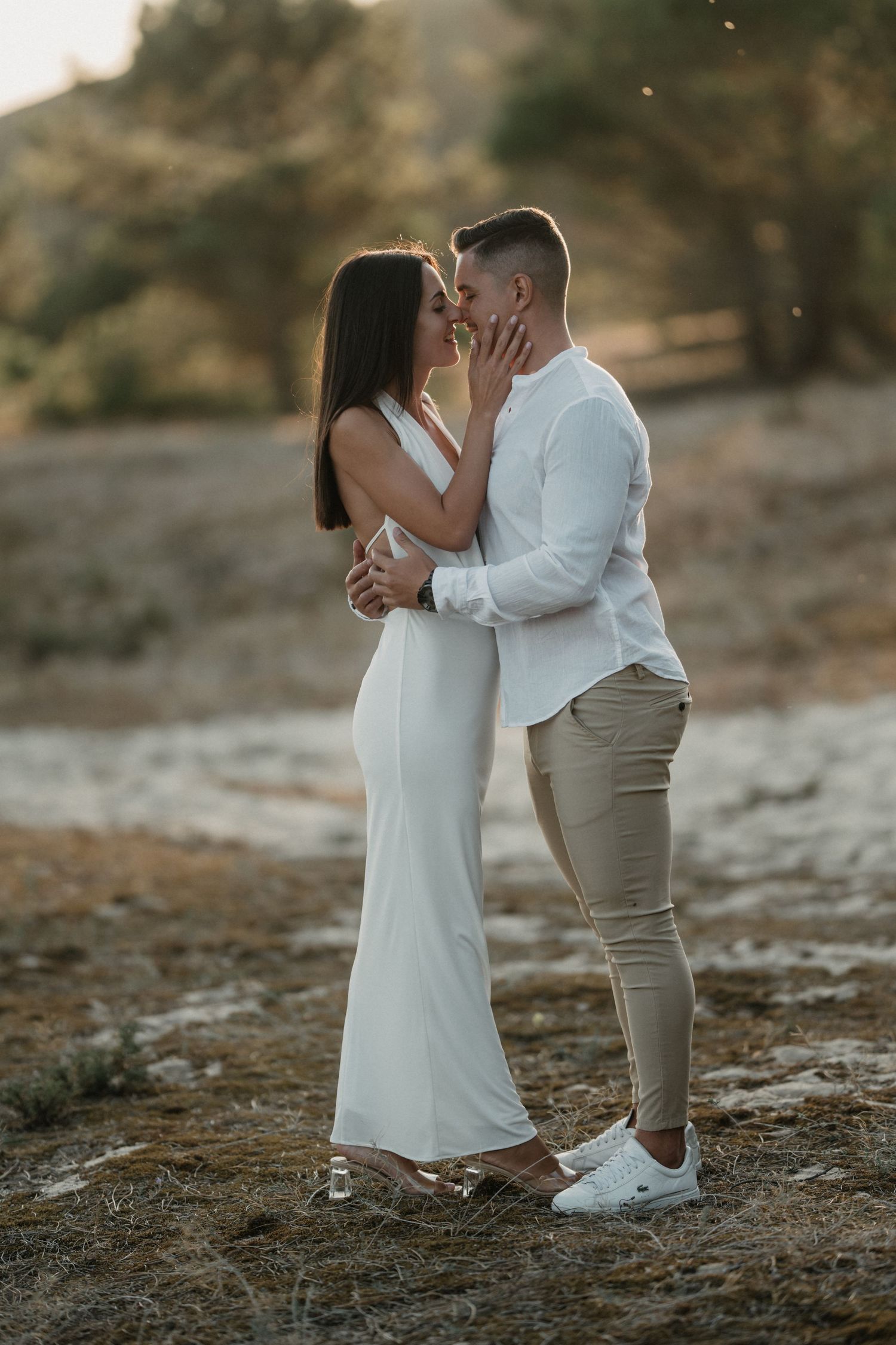 A romantic couple shares intimate moments while dancing together on rugged terrain at dusk.
