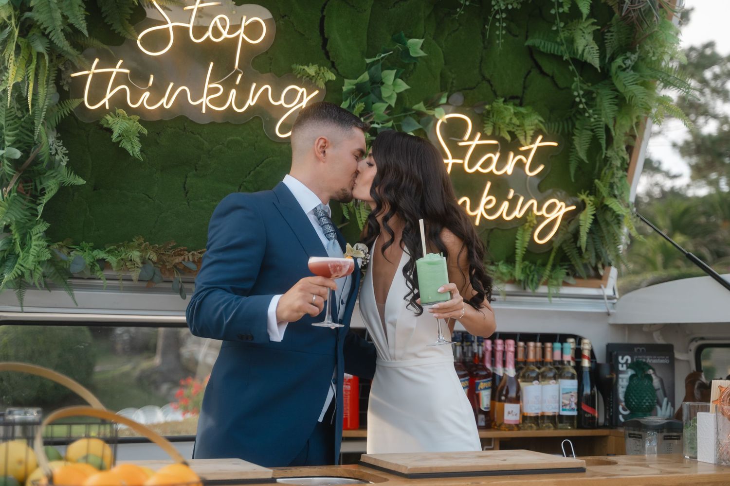 Illuminated neon signs spelling out words against green foliage at an outdoor event.