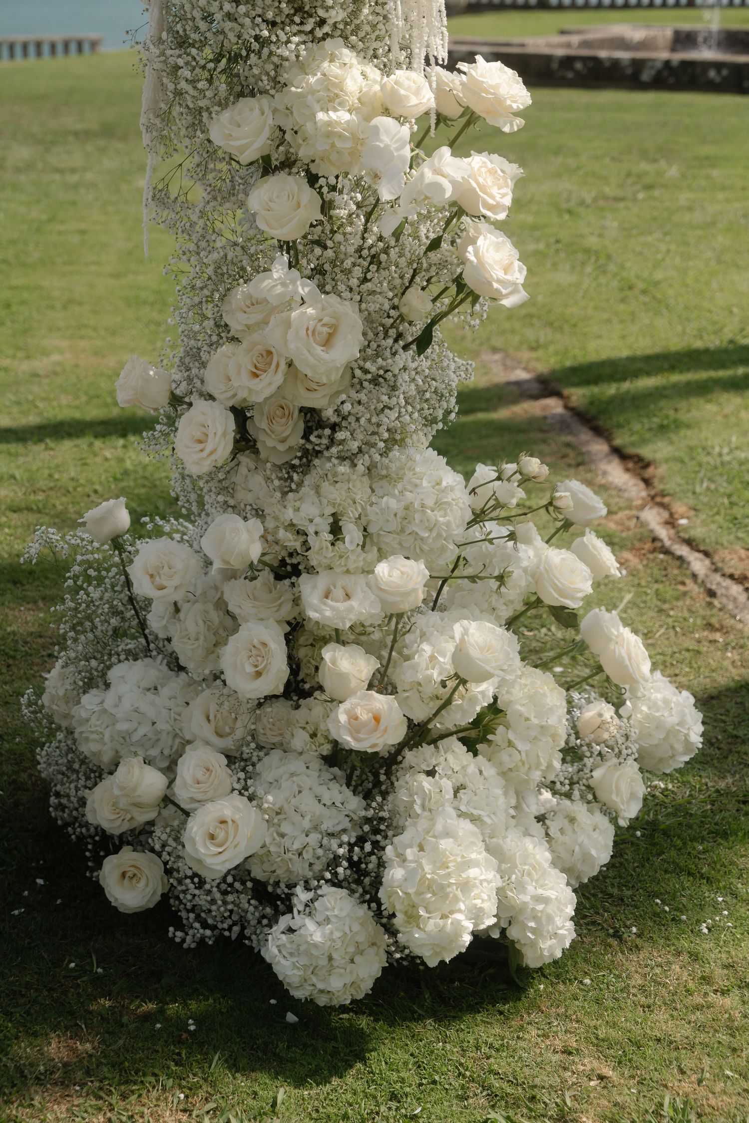 Lush white floral arrangements with roses and baby's breath decorating an outdoor garden space.