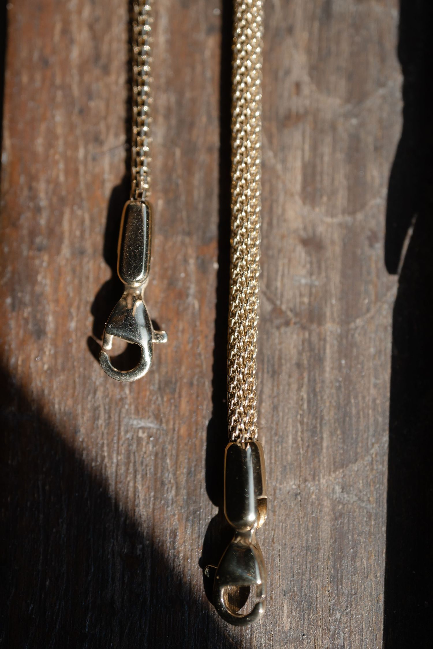 Gold chain necklace hanging against dark wooden background in dramatic lighting.