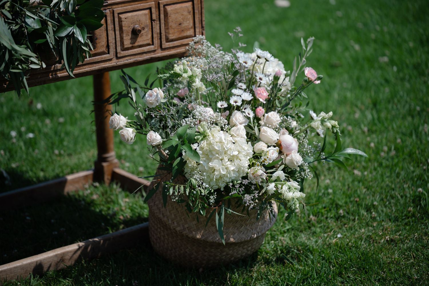 Rustic wooden cabinet decorated with white floral arrangements and greenery in an outdoor garden setting.
