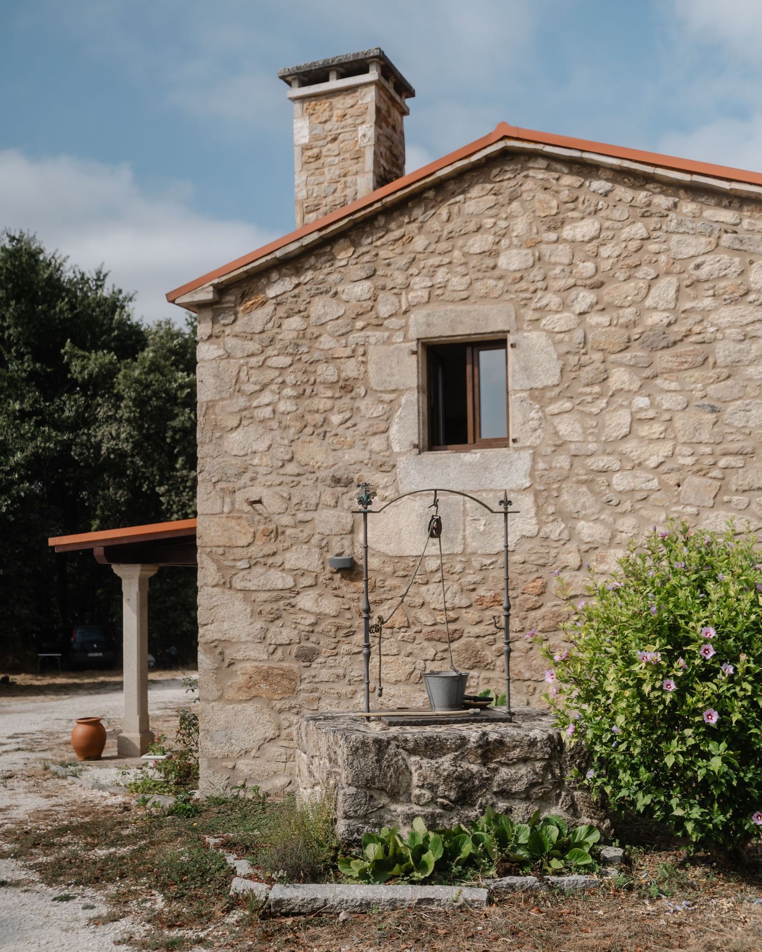 Rustic stone cottage with traditional well and chimney in Mediterranean countryside setting.