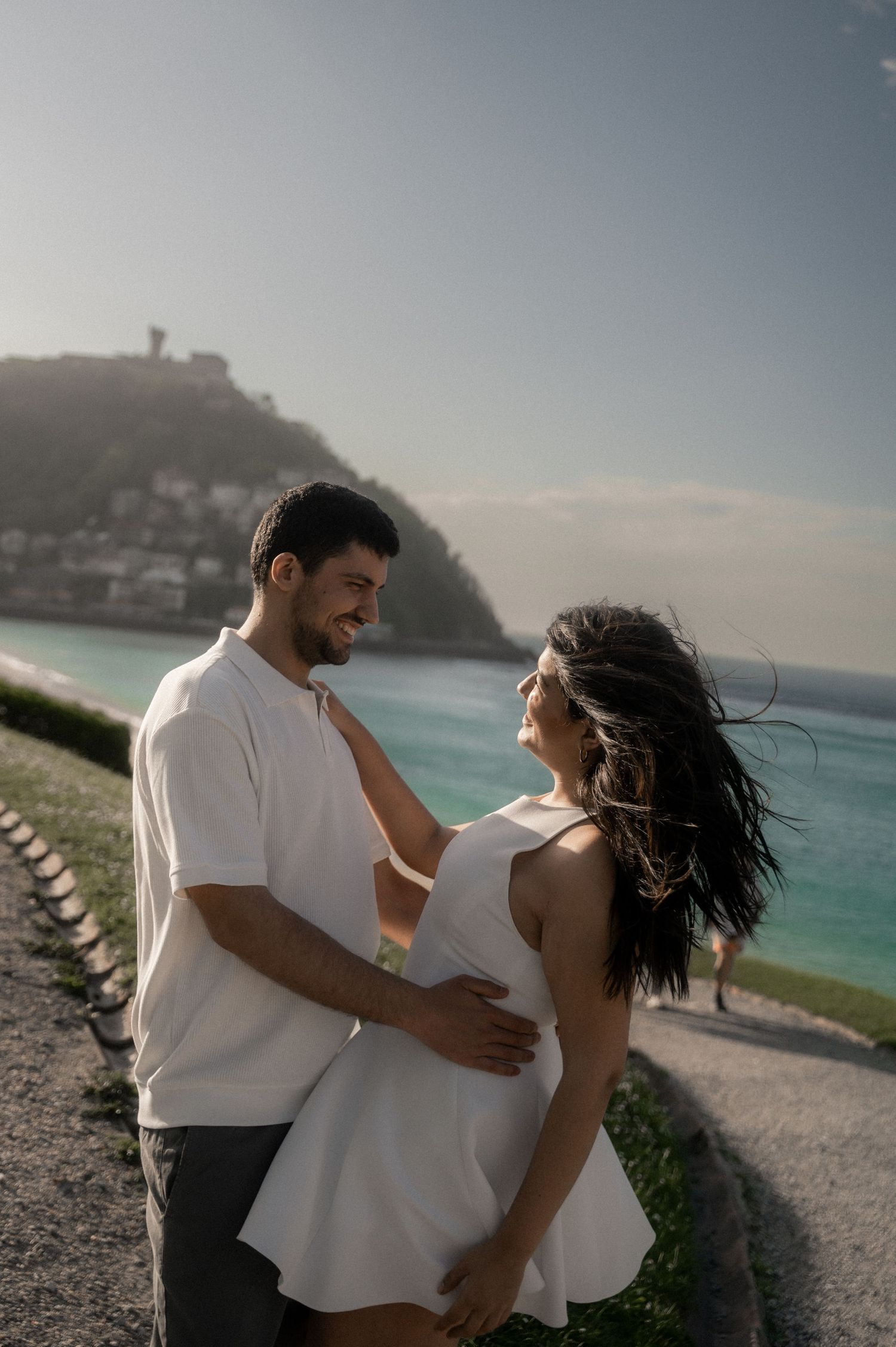 Couple sharing romantic moments on a scenic beach with turquoise waters and cliffs in the background.