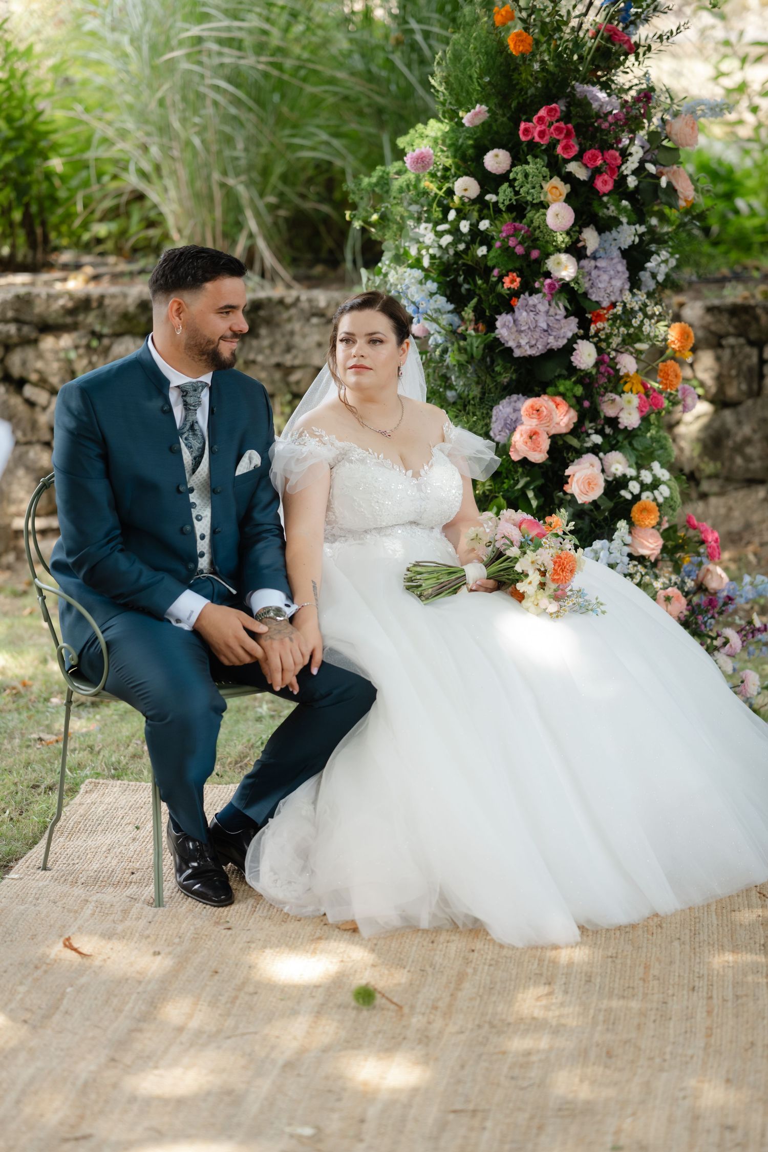 A couple shares an intimate moment on a brick patio surrounded by vibrant floral arrangements at their garden wedding.