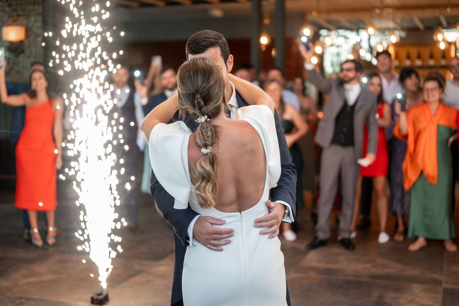 Newlyweds share their first dance at a wedding reception while indoor sparklers create magical light effects.