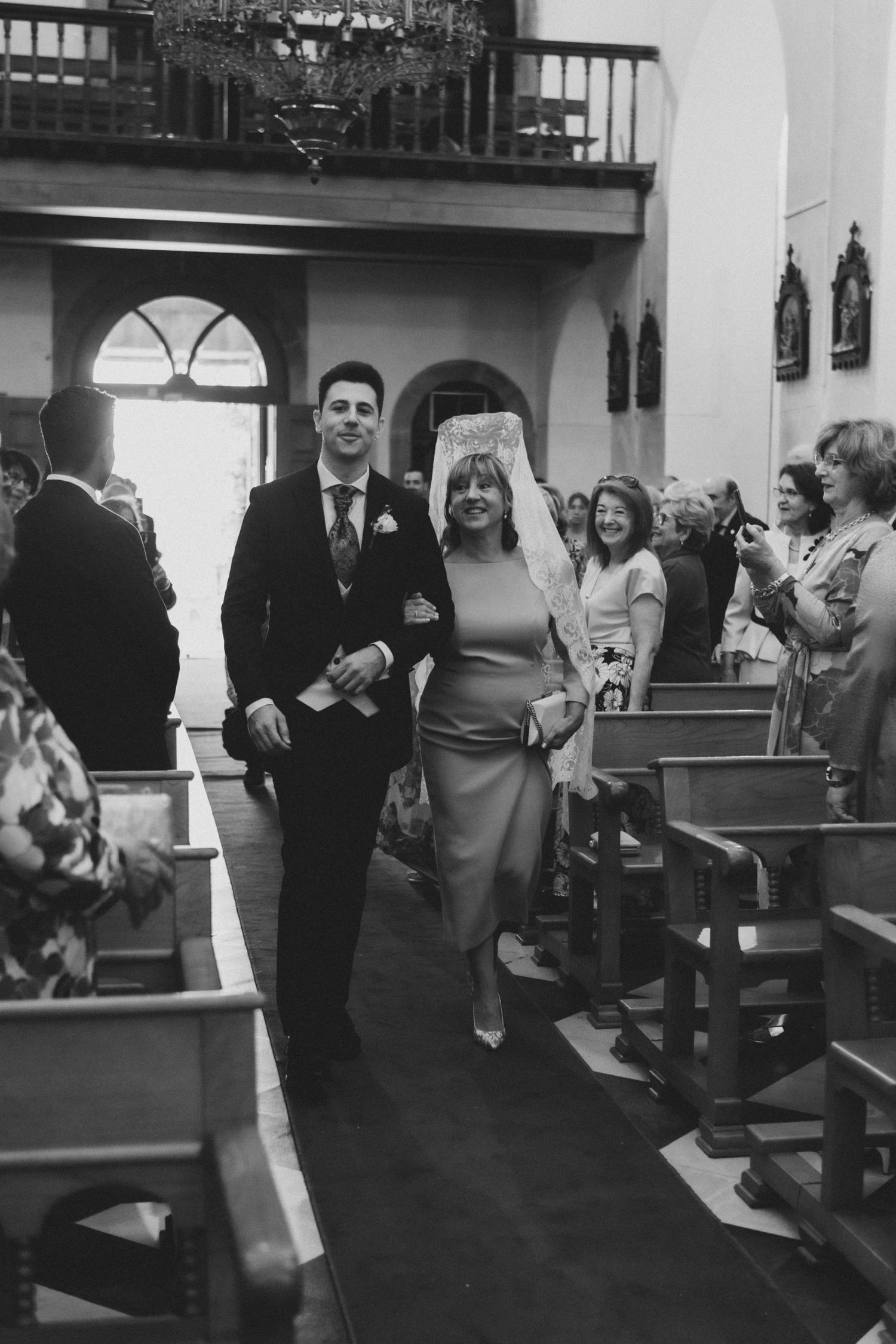 Black and white photo of a wedding ceremony in a church with guests seated in wooden pews.