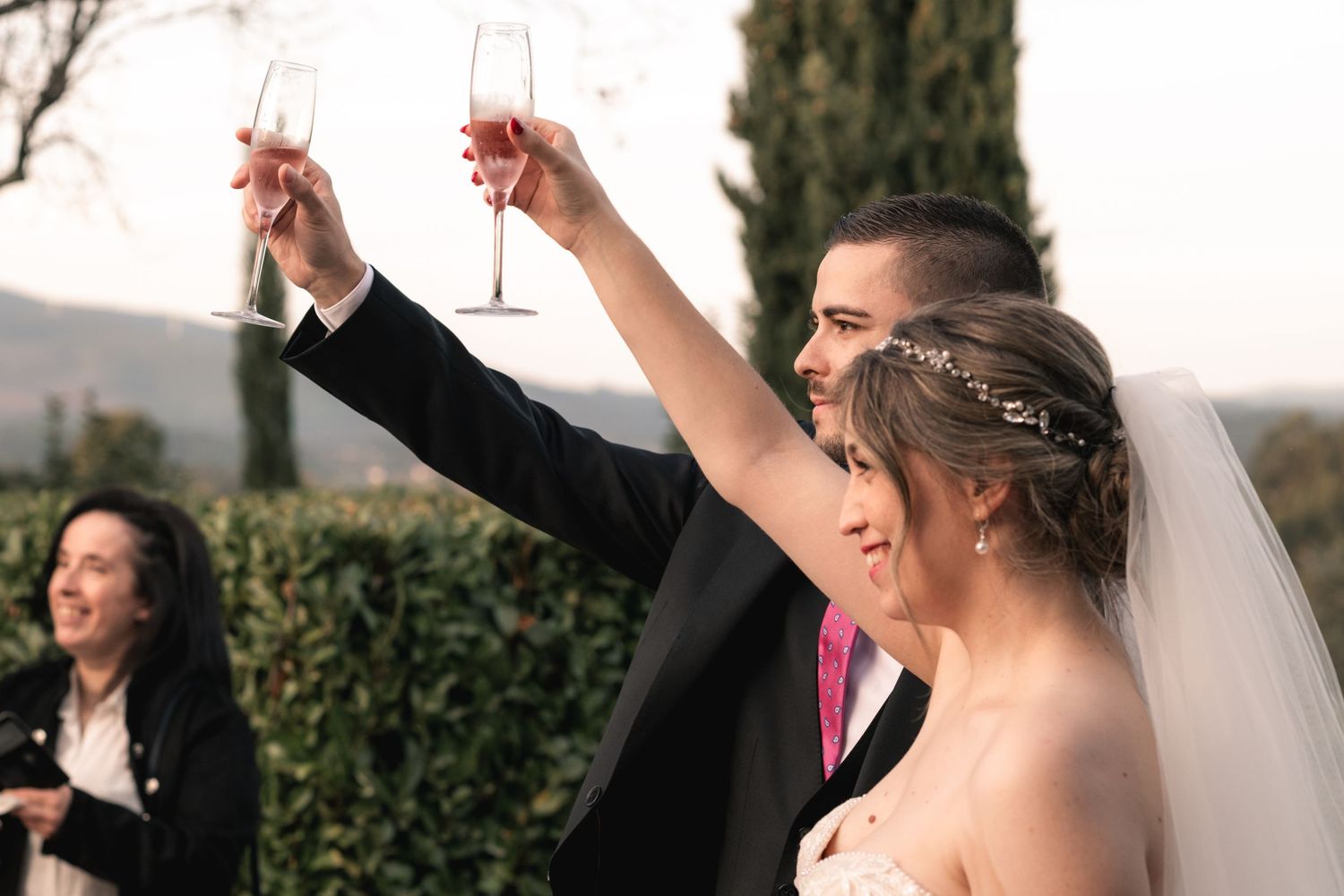 Joyful wedding celebration with dancing couples in formal attire and flowing veils outdoors.